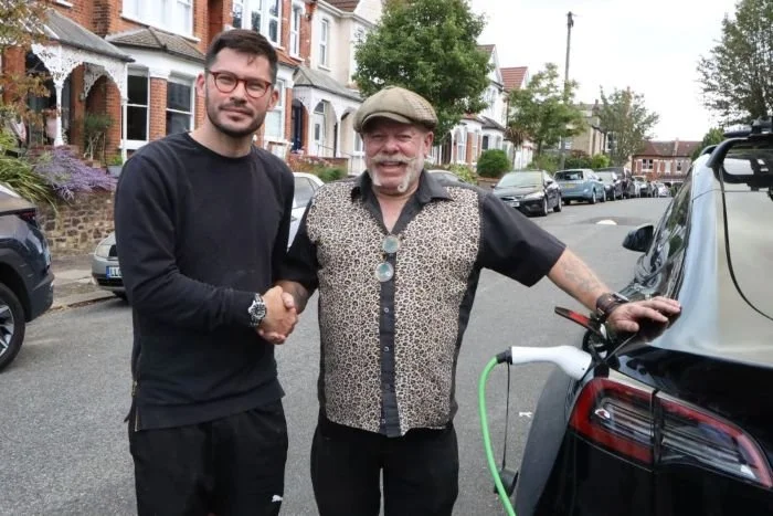 2 men shaking hands next to car being charged on the street