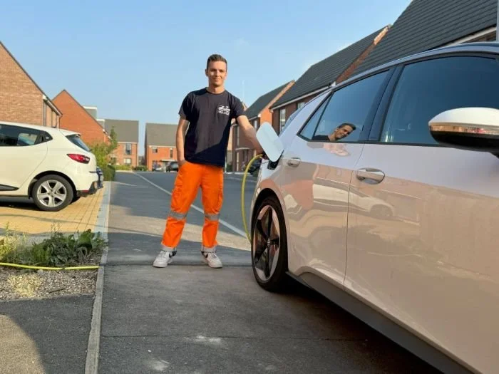 Man in high vis trousers charging EV while parked on street