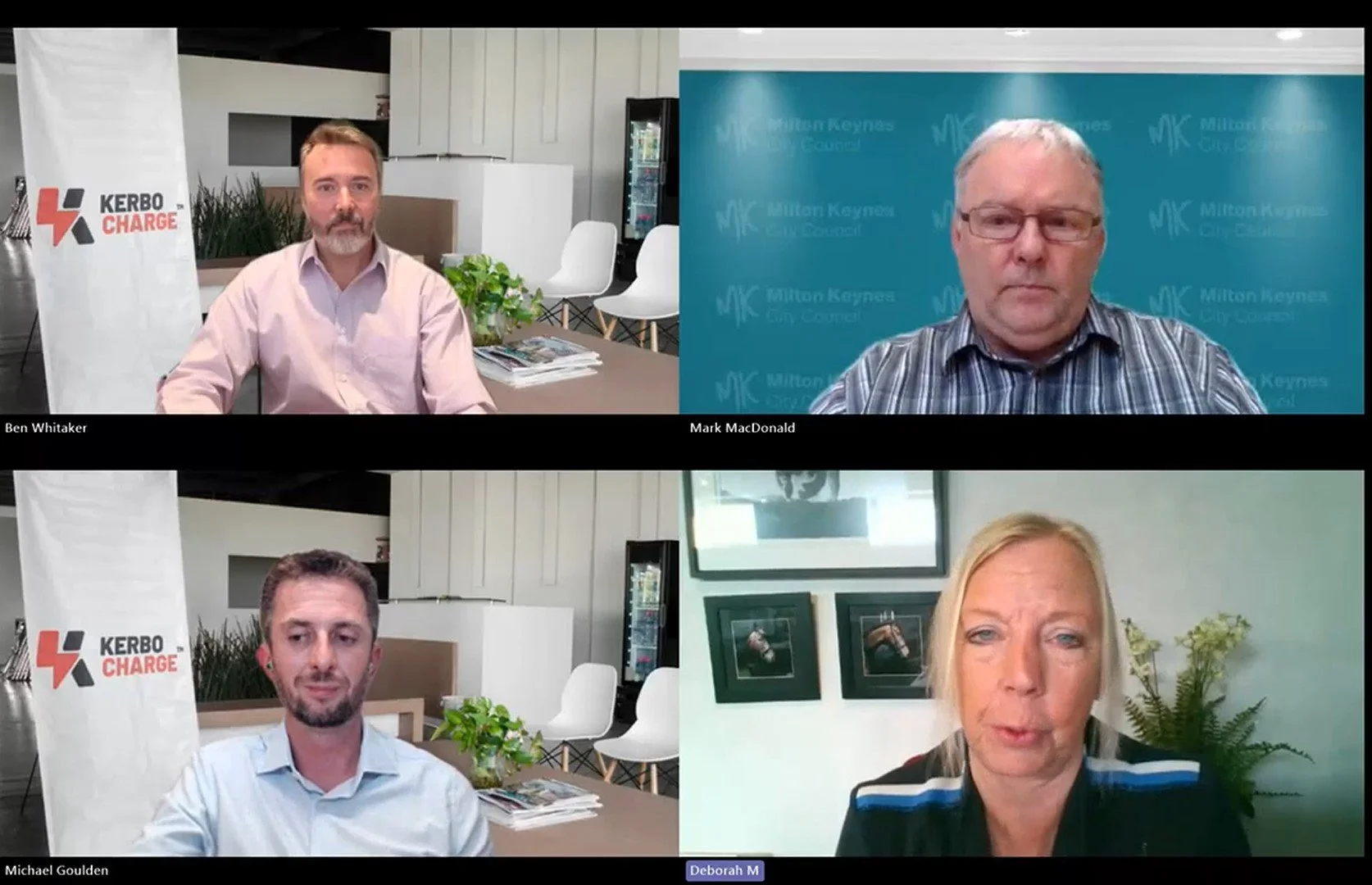 Four people participating in a virtual meeting, each in their own video call window. Top left: a man with a beard in an office with a Kerbo Charge banner. Top right: a man with glasses and gray hair against a blue background with Milton Keynes City Council branding. Bottom left: a man with short hair and a beard in an office with a Kerbo Charge banner. Bottom right: a woman with blonde hair, in a room with framed pictures of horses and a light-colored wall.