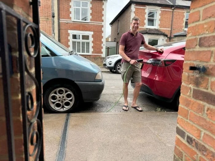 Man in tshirt, shorts and flip flops charging EV parked in the street using an EV cable gully installed in the pavement
