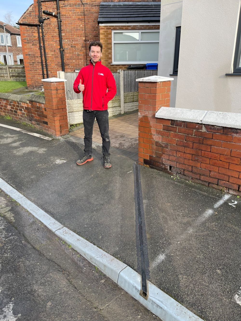 Man with thumps up standing on pavement next to a EV cable channel