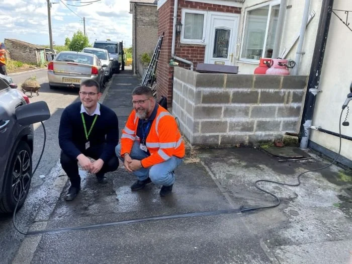 3 people stood on pavement next to EV being charged on the street