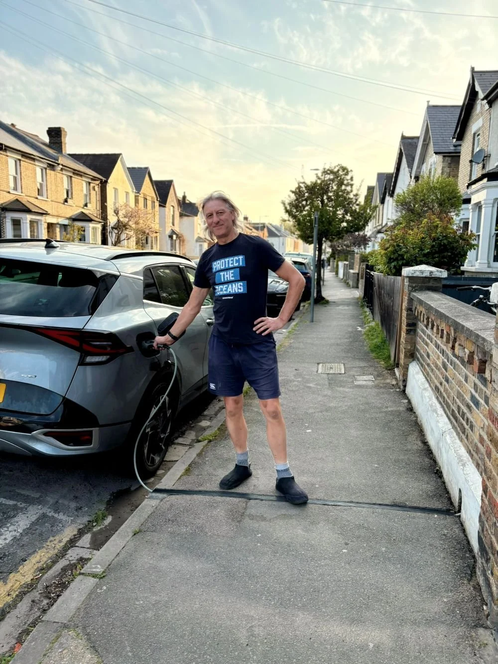 EV parked on residential street being charged by a man in shorts and tshirt