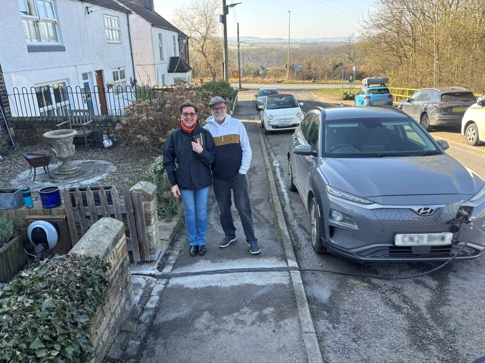 2 people stood on pavement beside charging car