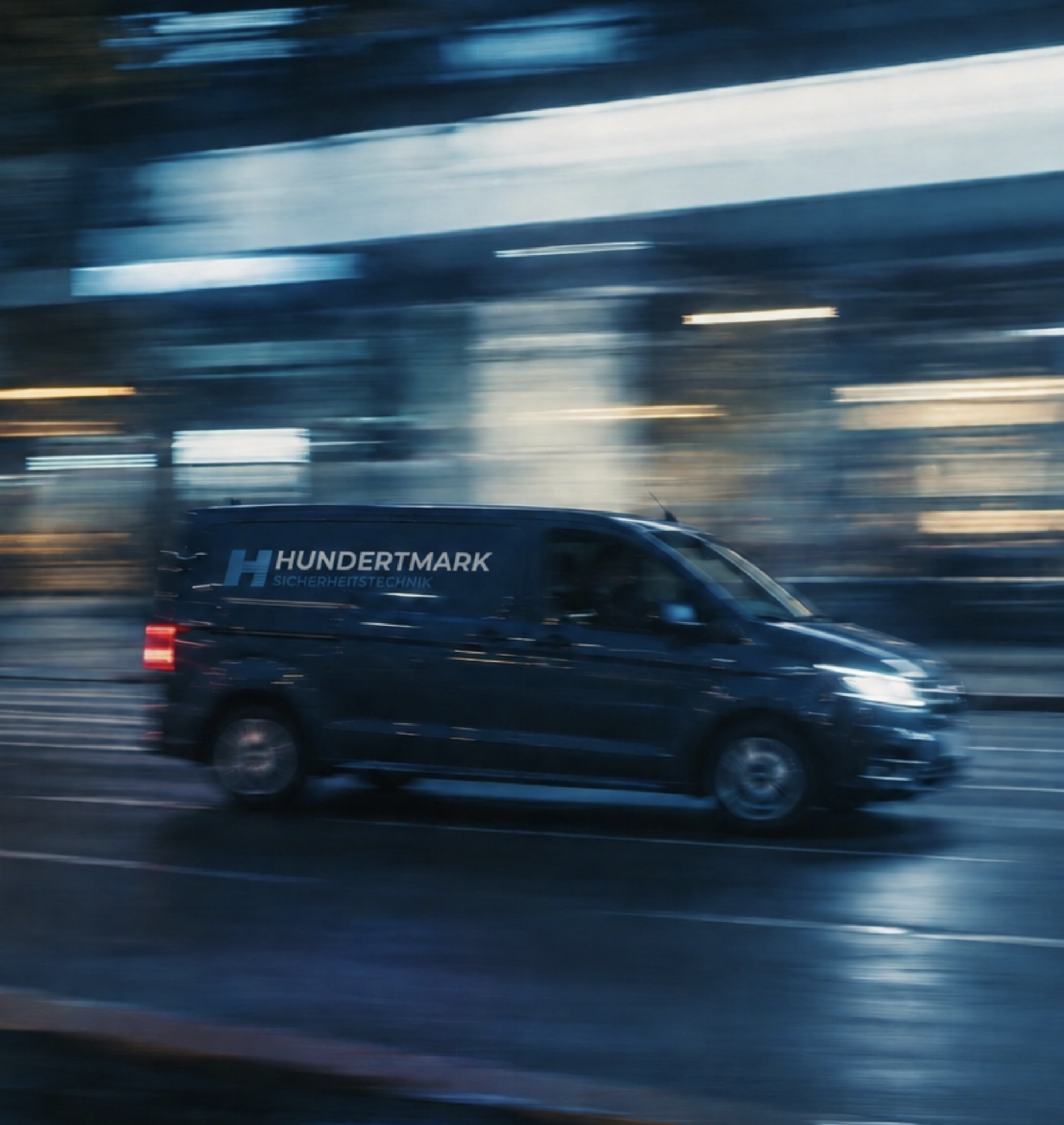 Black security technology service van labeled “Hundertmark Sicherheitstechnik” driving through a city at night in motion blur