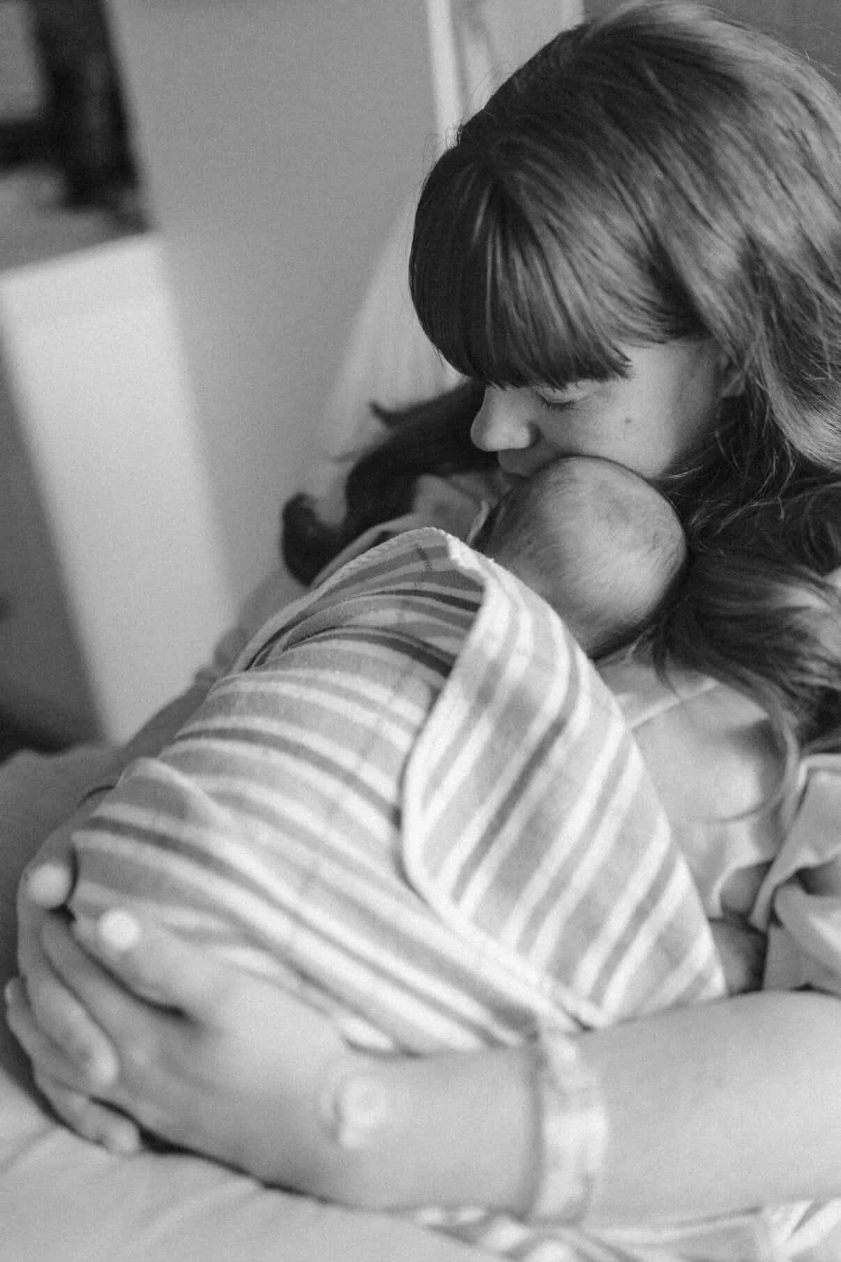 A woman holding and breastfeeding a baby, both wearing striped clothing, in a black and white photograph.