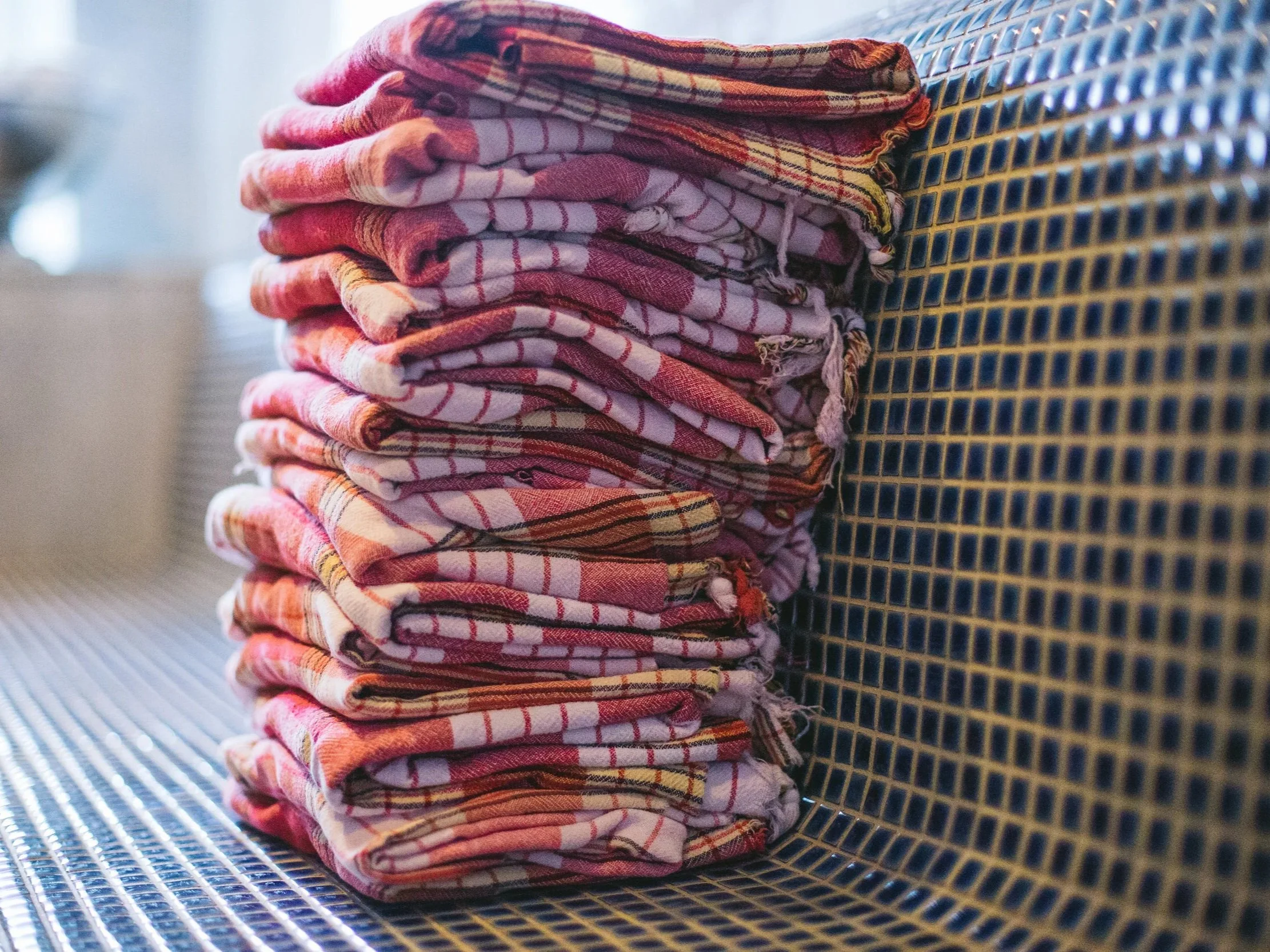 A neatly folded stack of red and white plaid cloths placed on a metallic surface with a blue and yellow grid pattern.