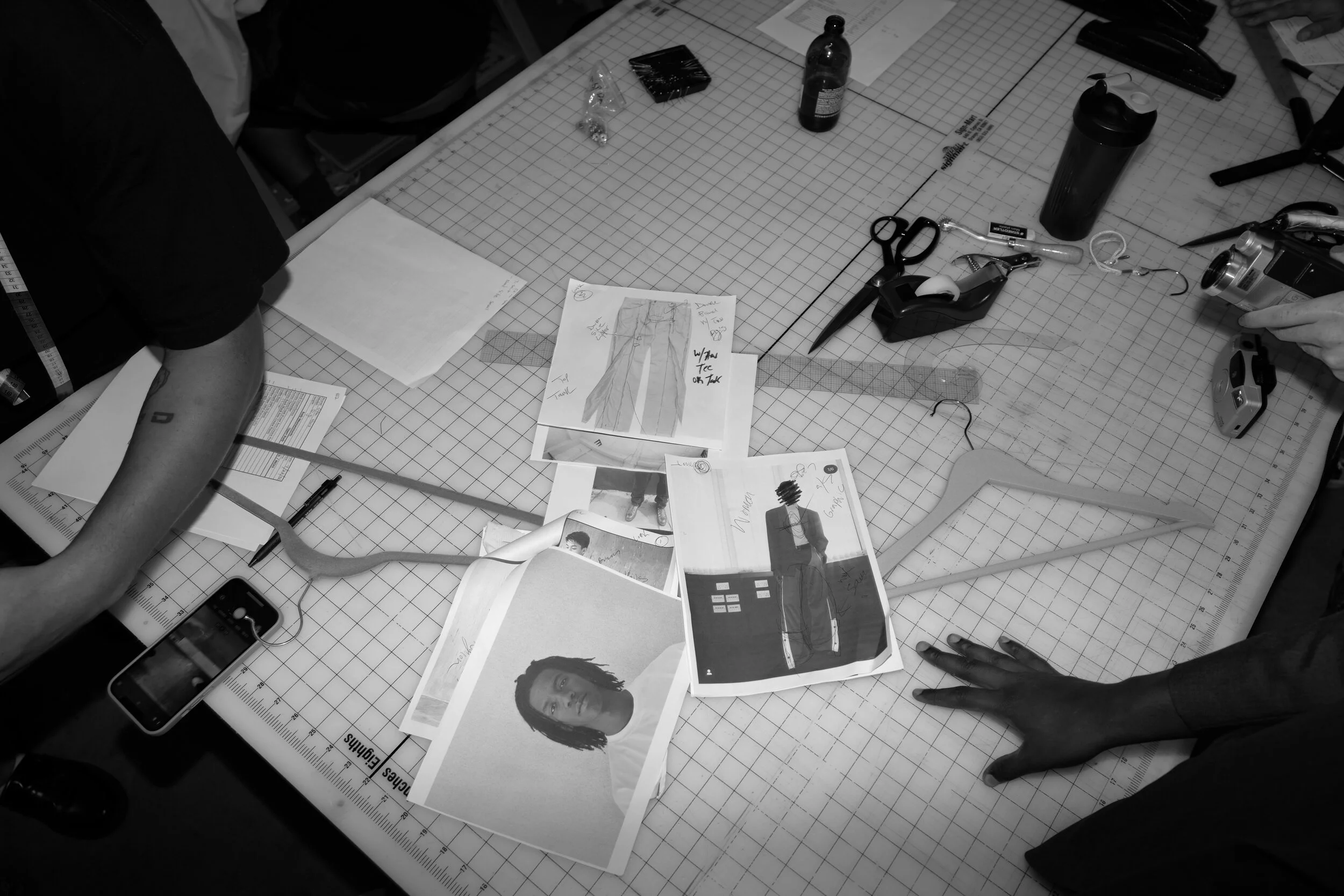 A cluttered workspace with photographs of a woman, papers, scissors, a tape dispenser, a camera, and various office supplies on a cutting mat.