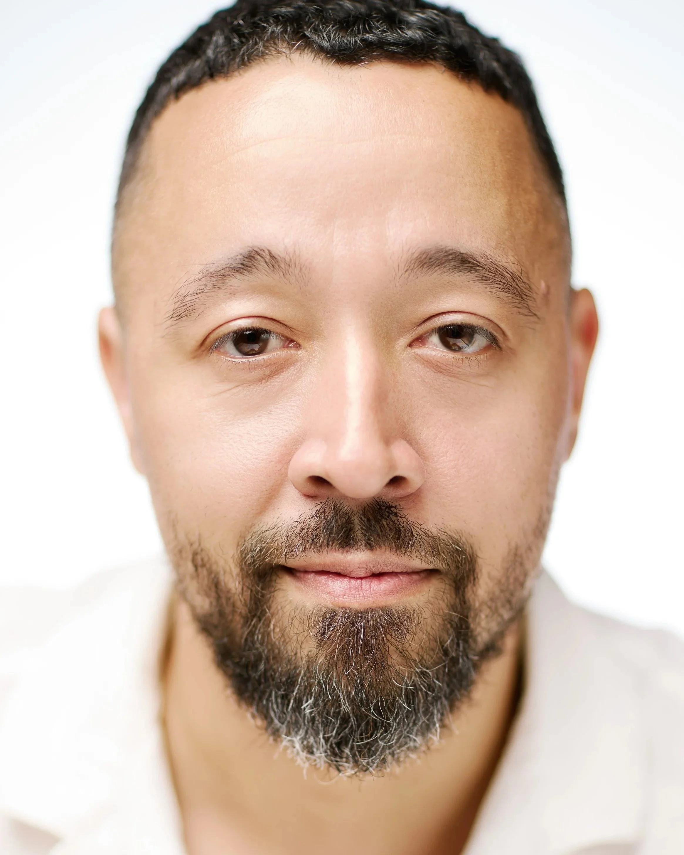 Close-up of a man's face, showing his forehead, eyes, nose, and beard, with short curly dark hair and a light brown complexion.