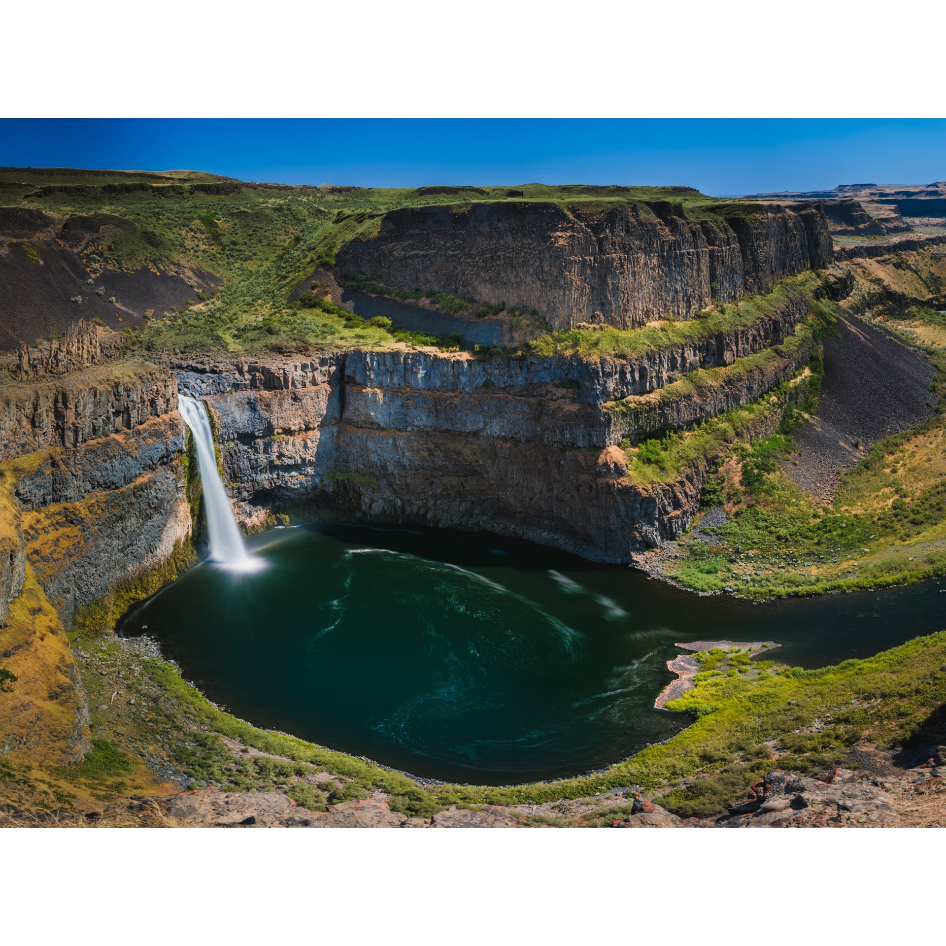 Aerial view of Palouse Falls plunging into a deep green pool.