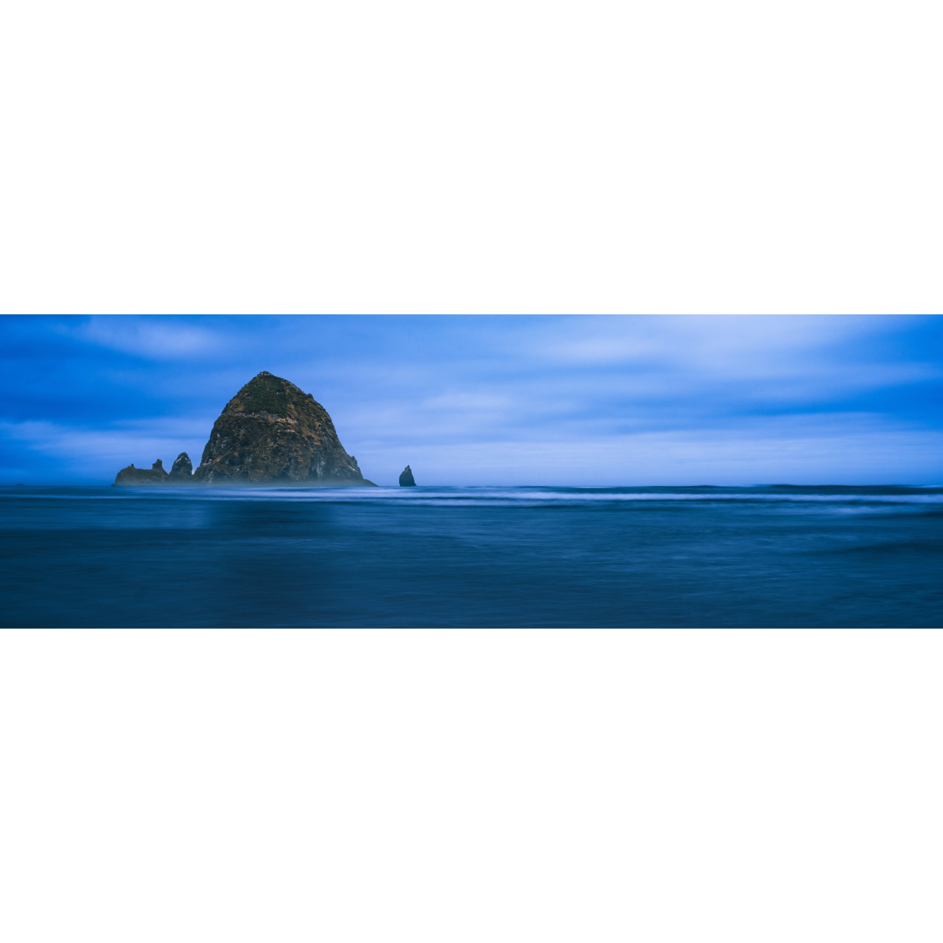 Iconic Haystack Rock emerging from a misty, blue ocean at dusk.