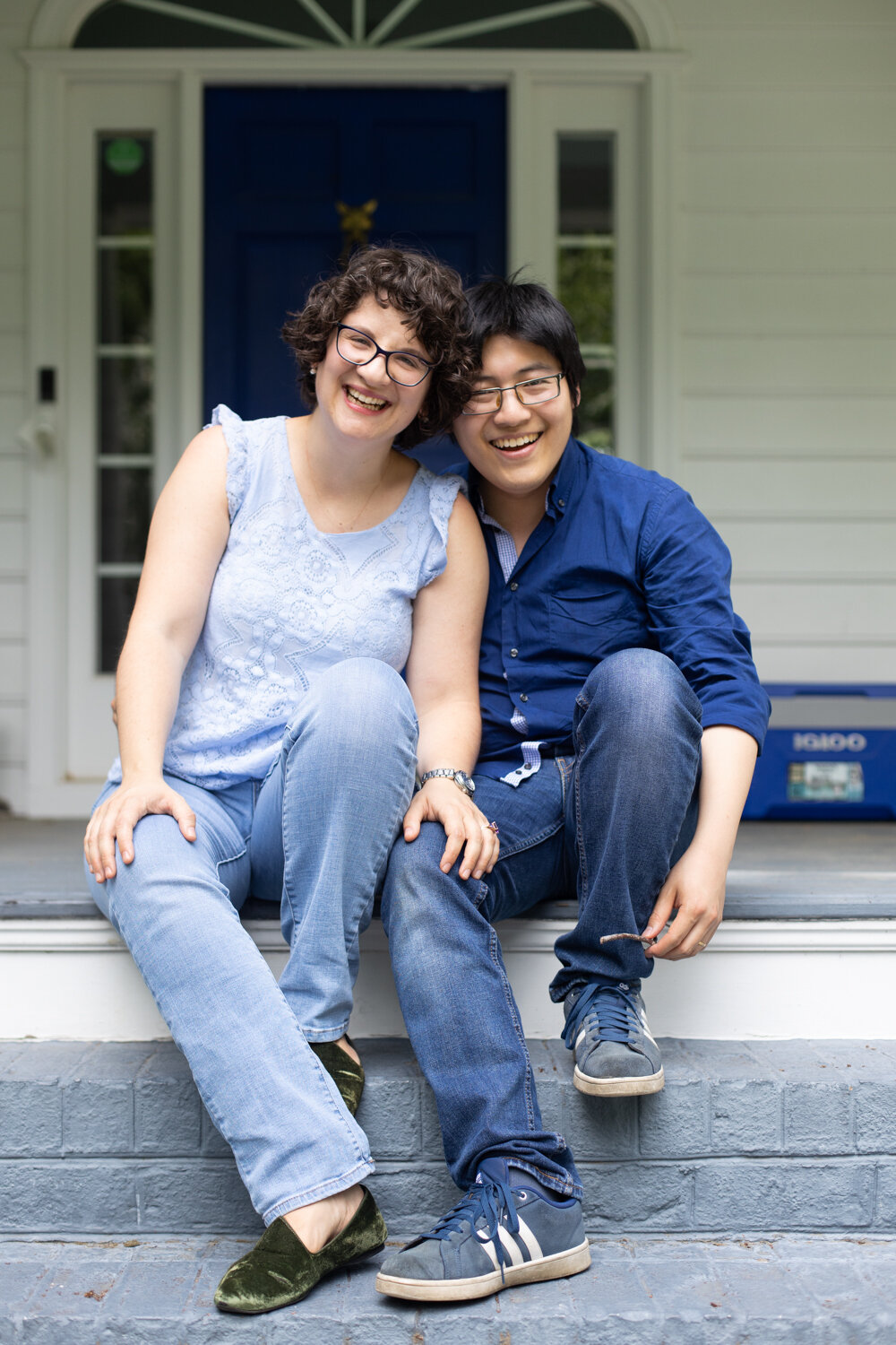 Couple sit on front steps and laugh together during family photo session