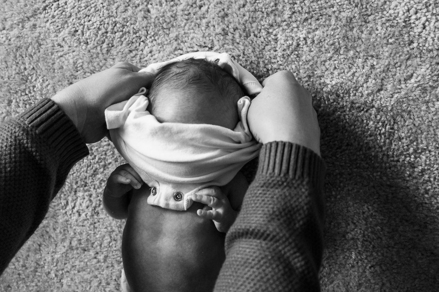  black and white image of a newborn having his clothing changed on the floor in his bedroom during his newborn photography session.  