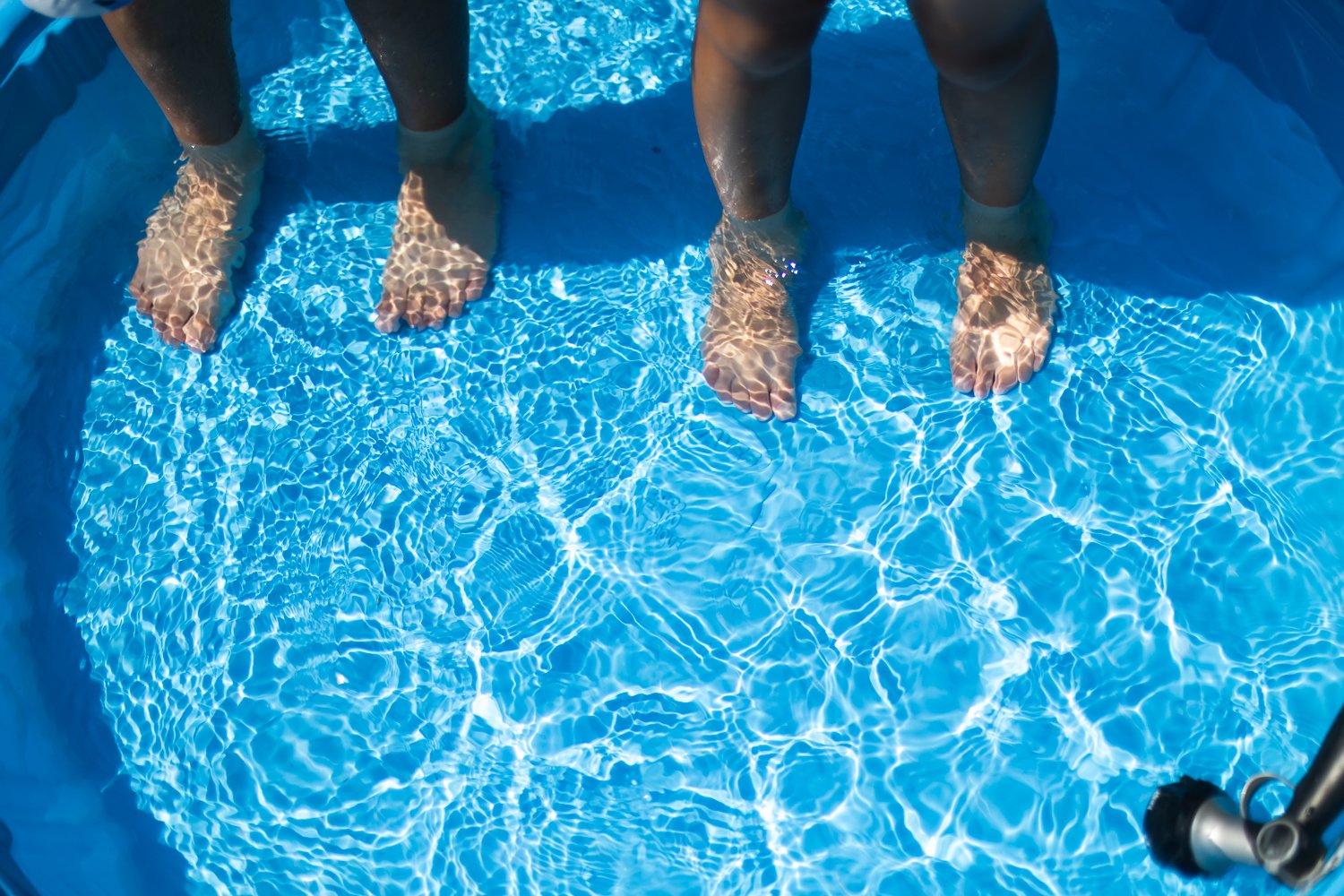 Two pairs of small children feet in ankle-deep water in a blue kiddie pool