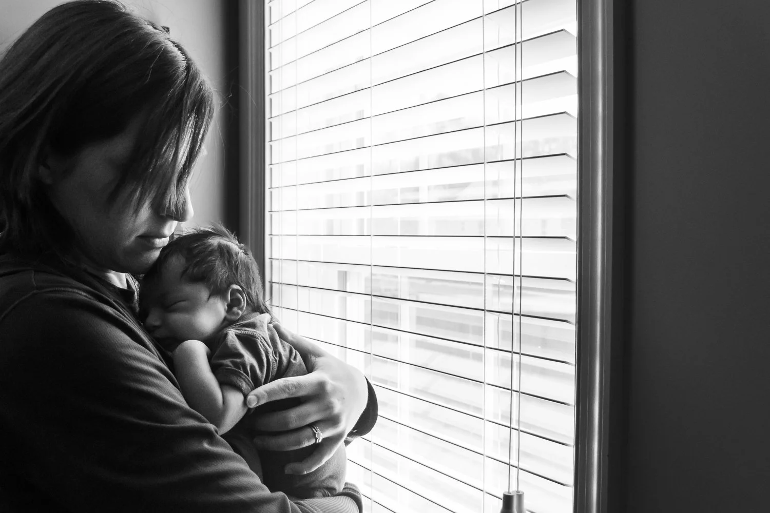 Allison Patel holding her newborn son beside the window at their home.