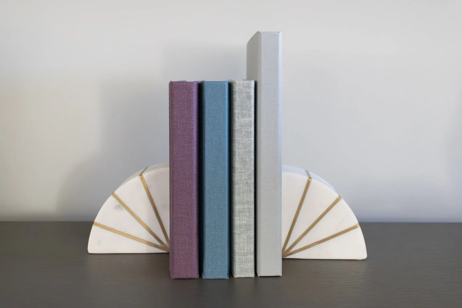 Four books standing upright on a shelf surrounded by white and gold bookends.