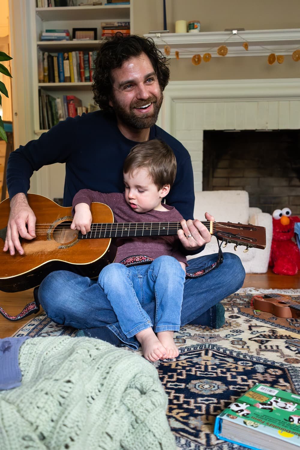 Father and son sit on their living room floor with a guitar.