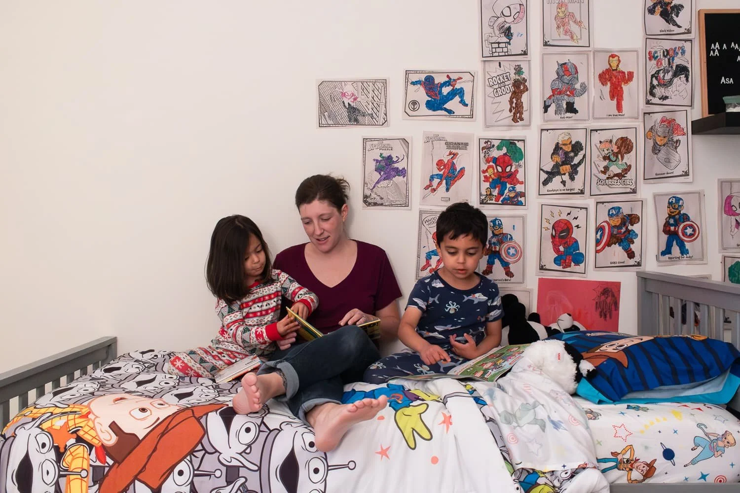 Allison Patel reads bedtime stories with her kids on her son's bed. The kids are little, in pjs, the bed covered in Toy Story bedding and the wall covered in Avengers coloring pages.