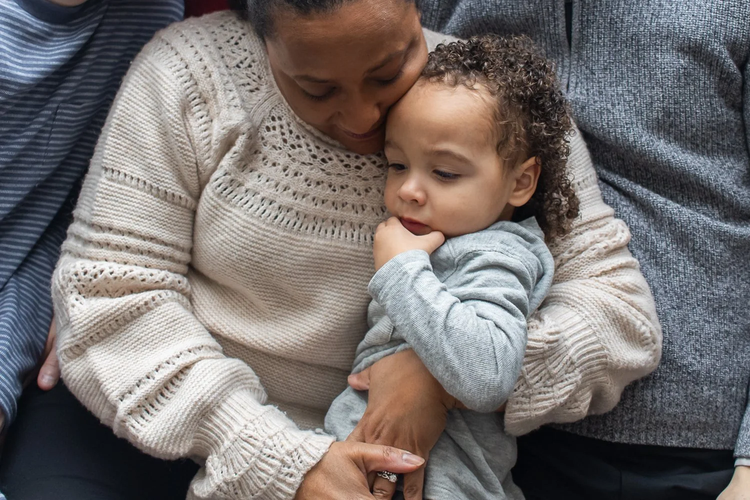 Mom snuggles her little boy on the couch, surrounded by other family members.