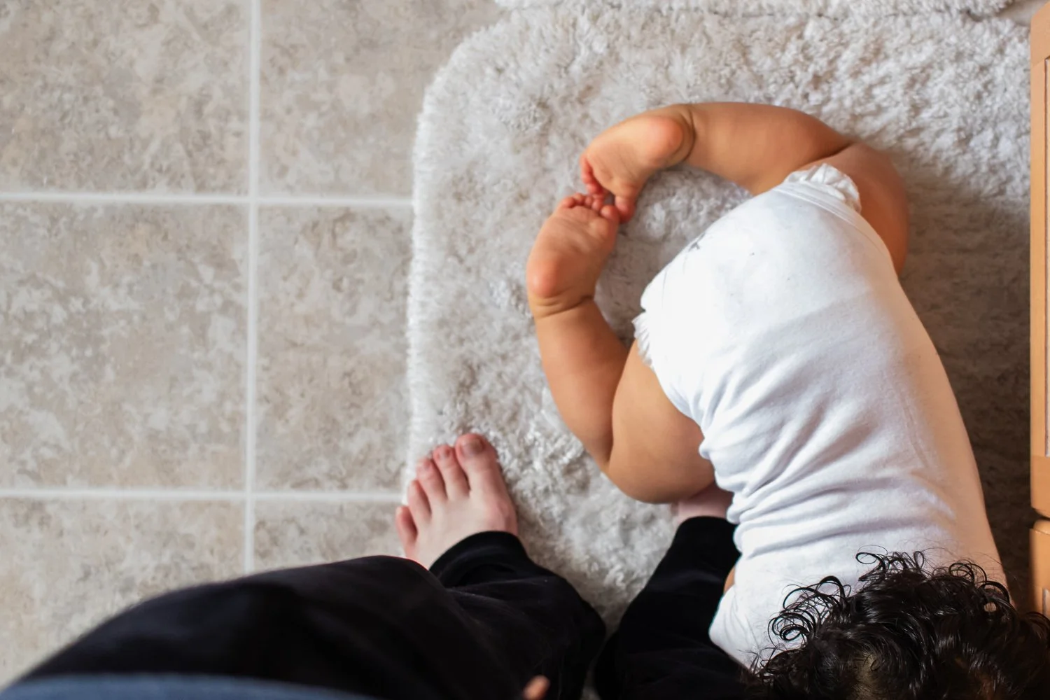 The legs and back of a crawling baby, around the mother's feet.