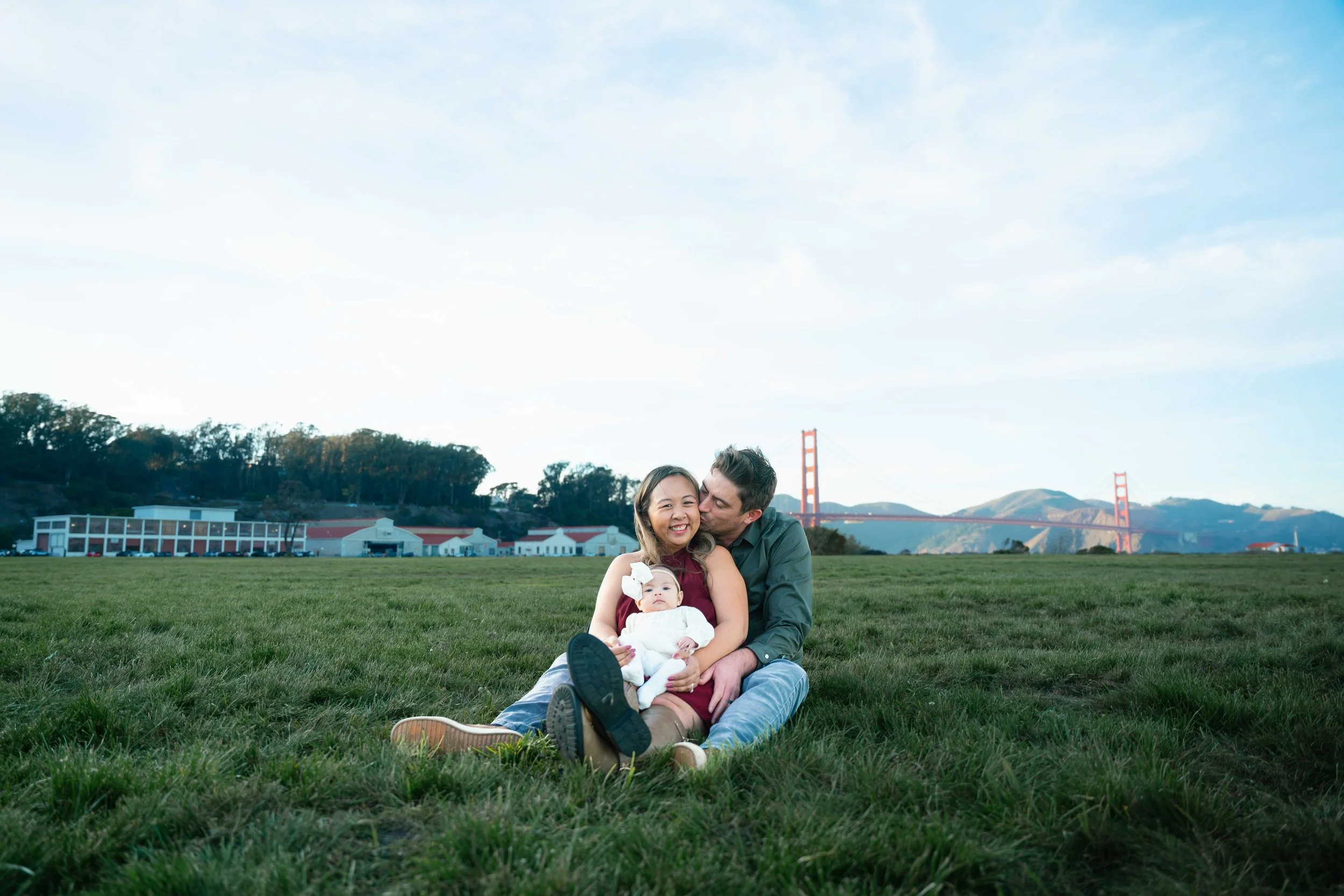 Family sitting on grass with the Golden Gate Bridge in the background, smiling and enjoying the outdoors.