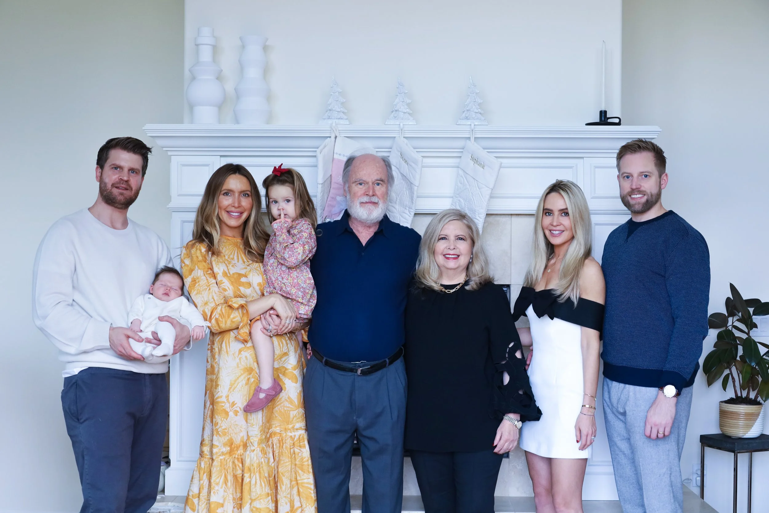 Family portrait with eight members standing in front of a fireplace with holiday stockings and decor.