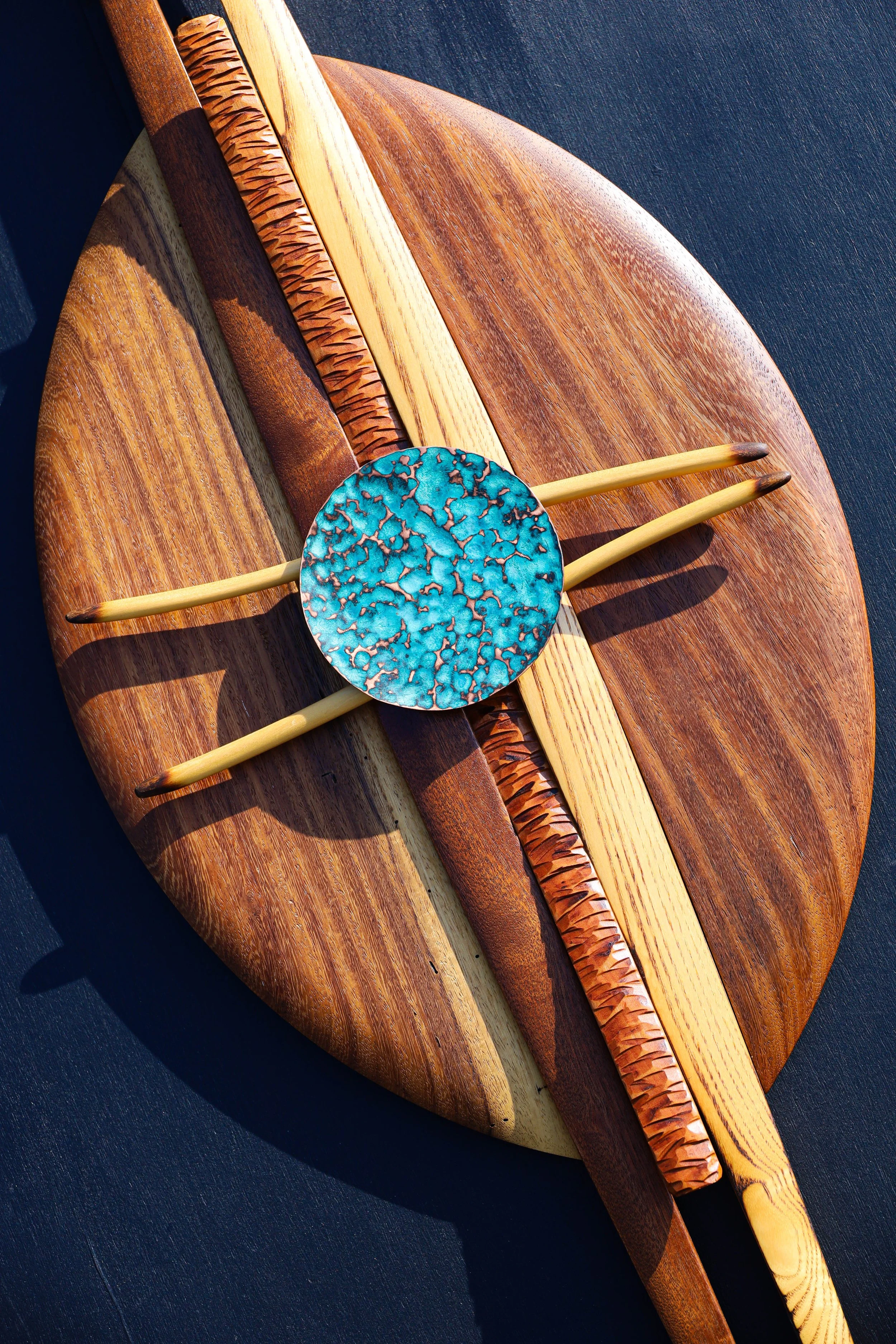 Decorative wooden art piece with a circular turquoise ceramic element, two bamboo sticks, and various carved wooden accents on a dark surface.