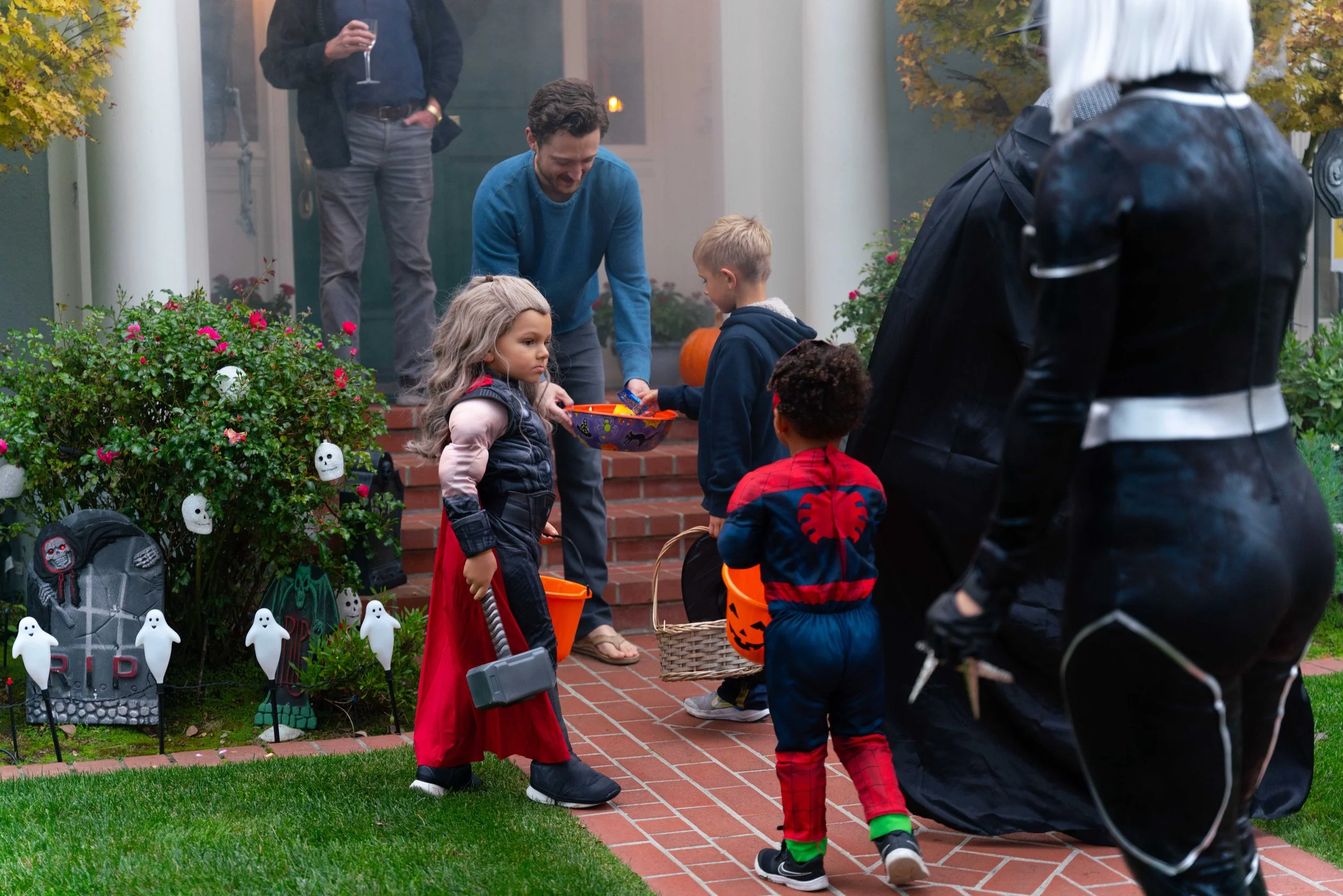 Kids in costume trick-or-treating at a house decorated with Halloween decorations, while adults supervise.