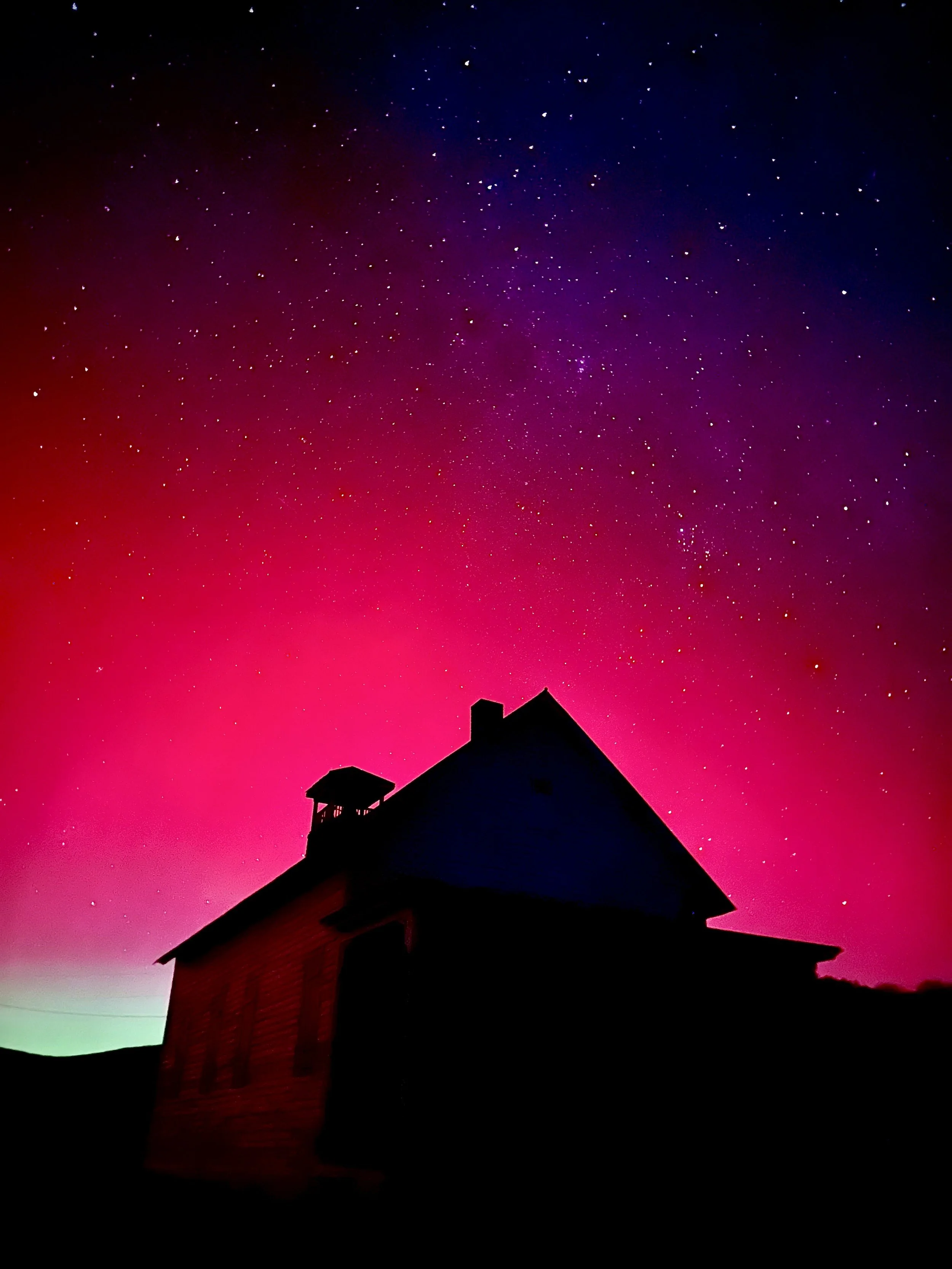 Silhouette of a house with a chimney under a colorful night sky filled with stars and a gradient of pink, purple, and green hues.