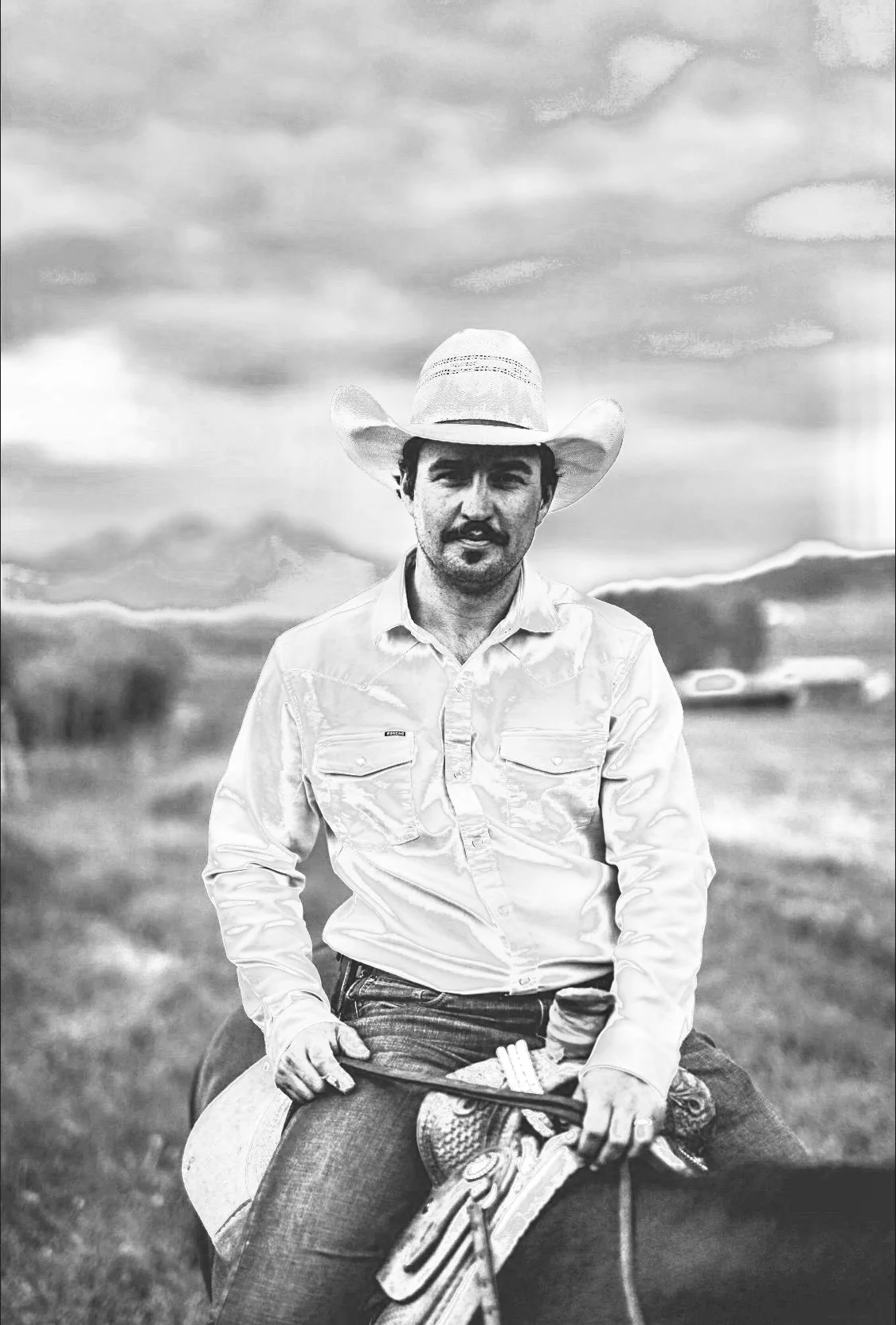 Black and white photo of a man wearing a cowboy hat and a button-up shirt, sitting on a horse, with mountains and clouds in the background.
