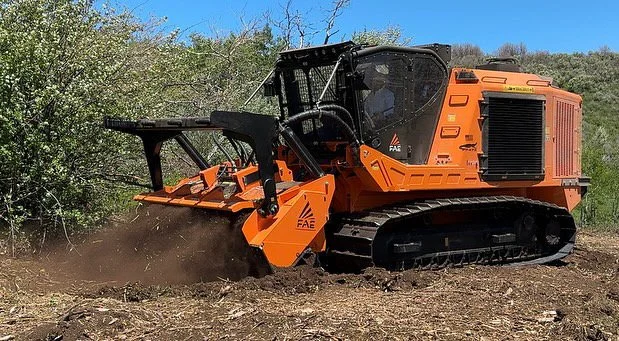 An orange bulldozer working on a dirt area with trees and a clear blue sky in the background.