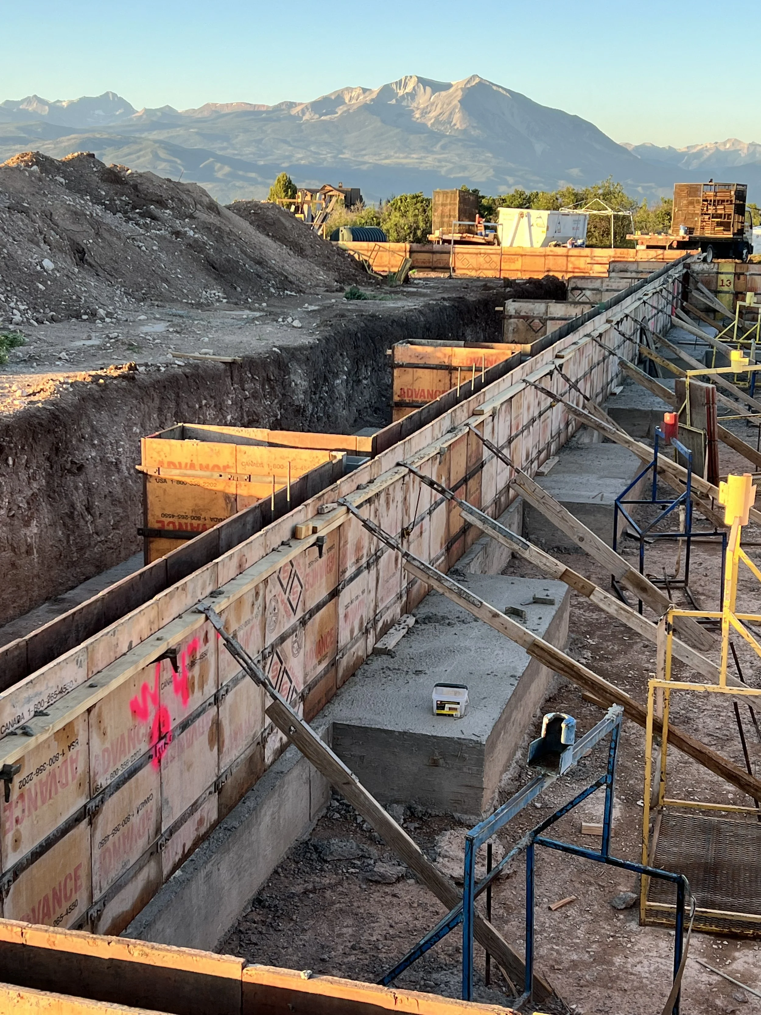 Construction site with a trench, wooden support beams, and safety barriers with mountains in the background.