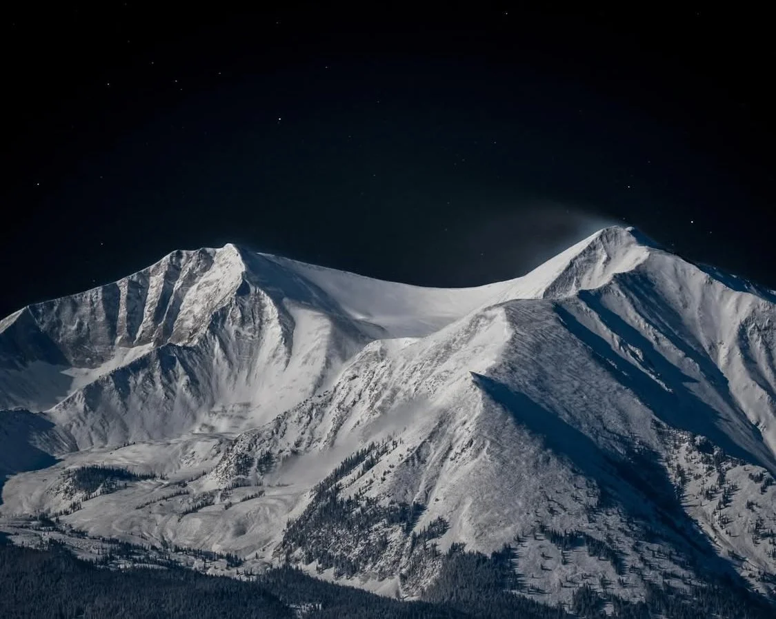Snow-covered mountain peaks under a starry night sky.