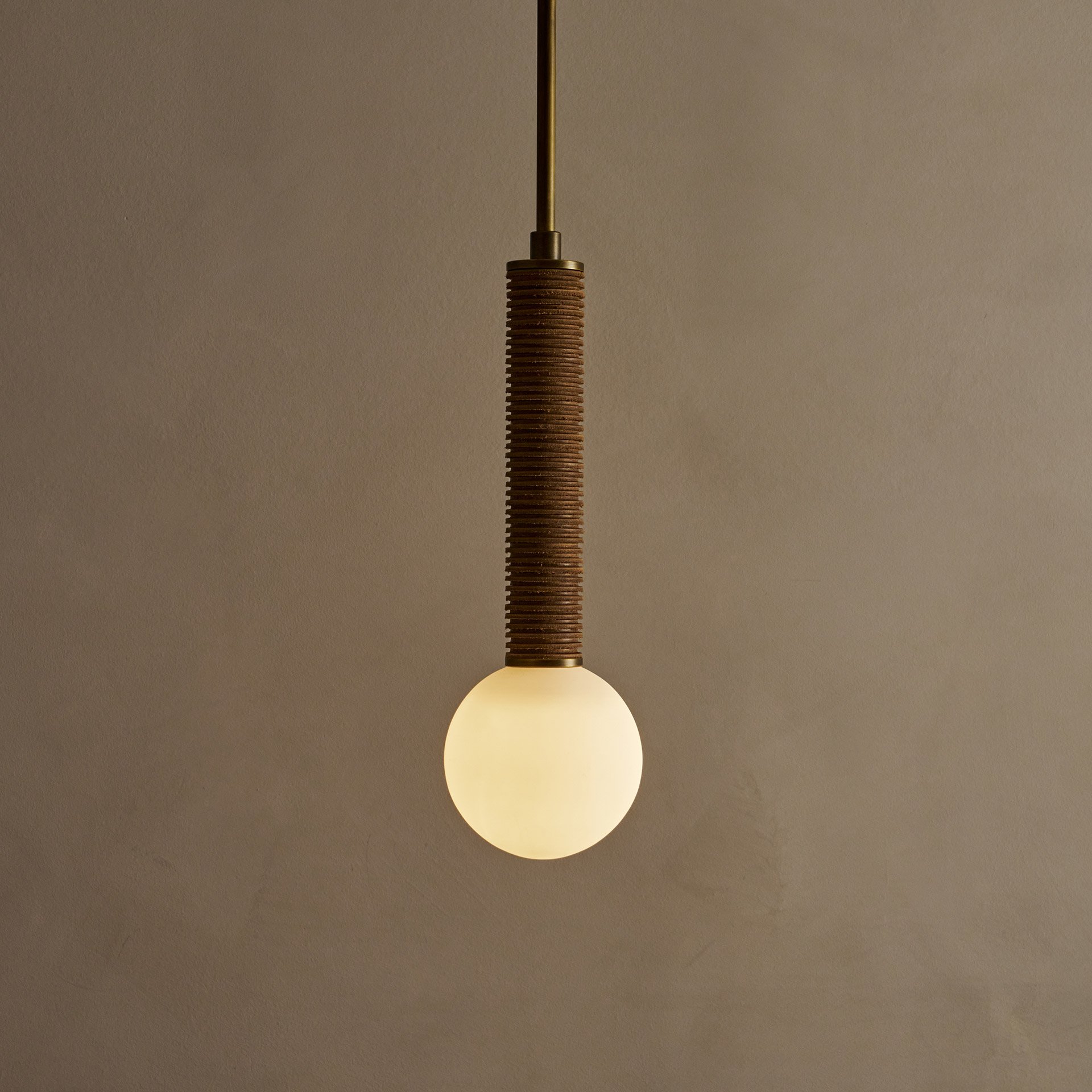 The Pell pendant lamp features a solid body crafted from stacked leather hide disks, showcasing the natural imperfections of the material's edge. A frosted glass sphere hangs at the bottom.