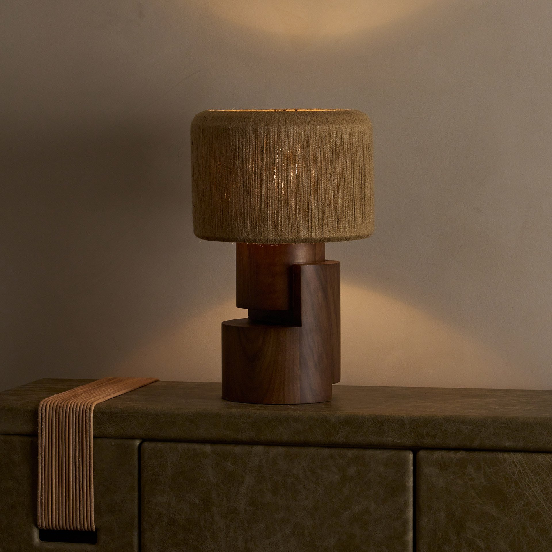 The Stagg table lamp showcases stacked wood cylinders supporting a brass frame with a handwoven string shade, revealing both symmetric and asymmetric forms from different angles.