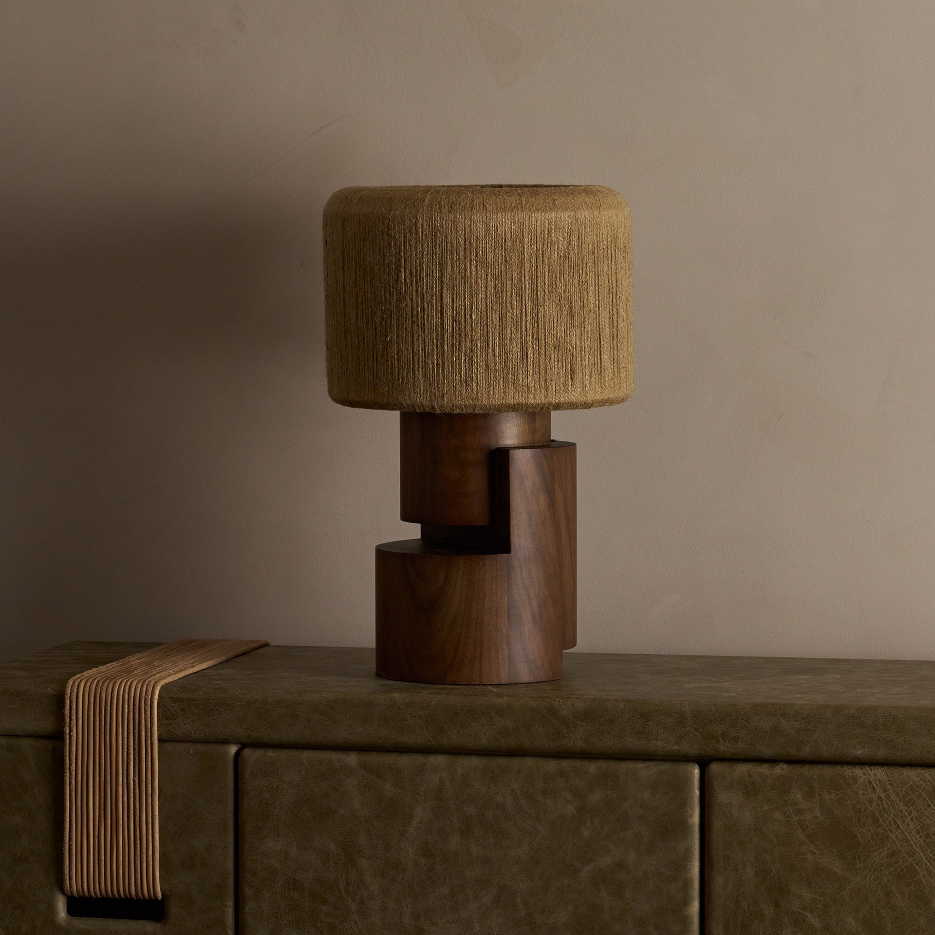 The Stagg table lamp showcases stacked wood cylinders supporting a brass frame with a handwoven string shade, revealing both symmetric and asymmetric forms from different angles
