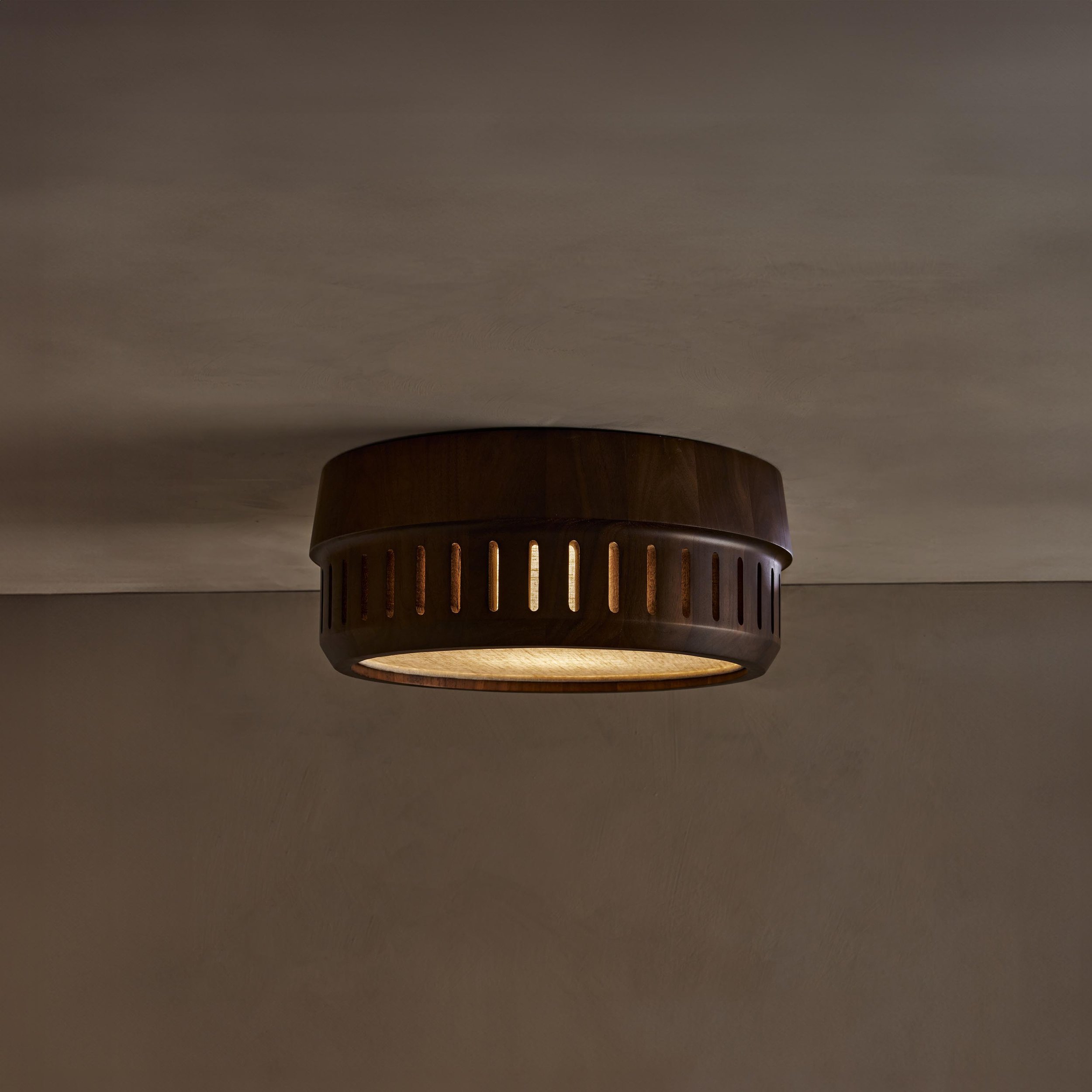 The Adler ceiling mount nests a linen drum shade within a solid wood exterior, offering functional downward illumination. Notches in the wood allow glimpses of the fabric shade within.