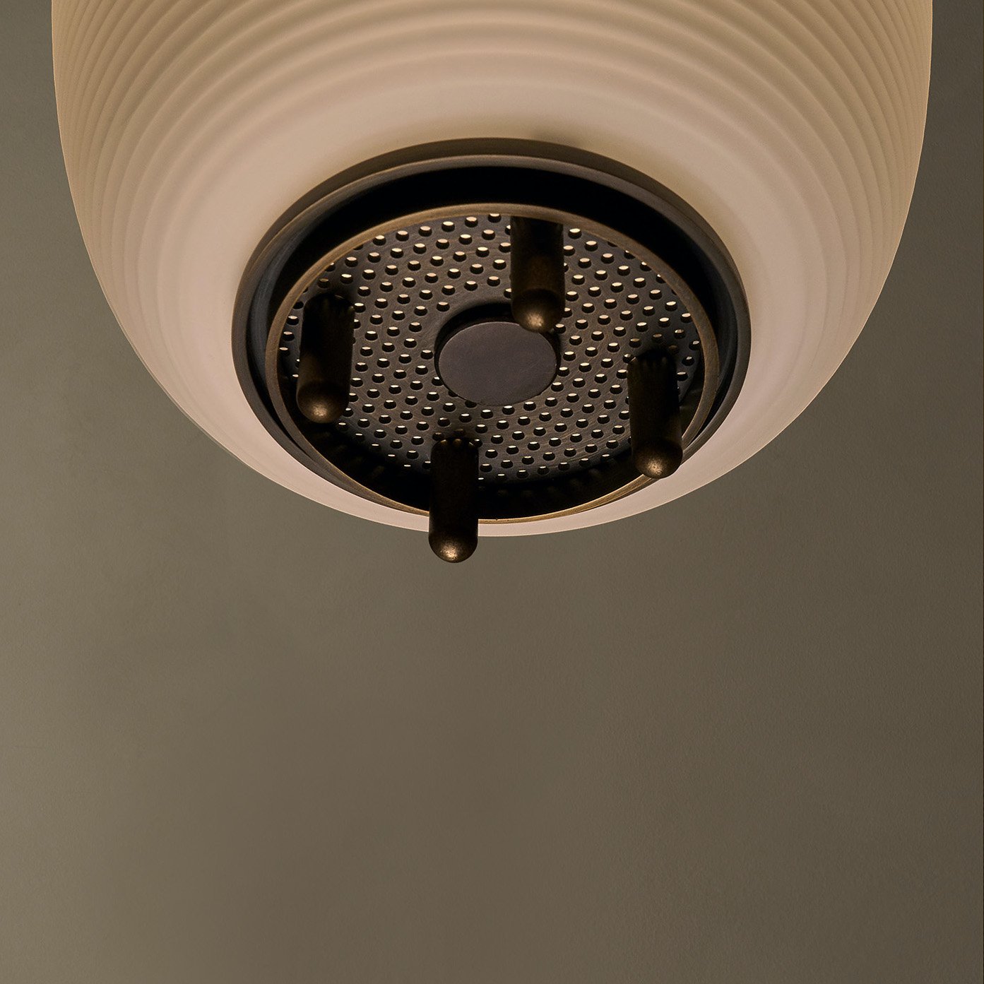 The Milton ceiling pendant embodies fluid design with solid brass and reeded glass elements. Supporting bars extend through, converging at a perforated brass plate for a seamless aesthetic