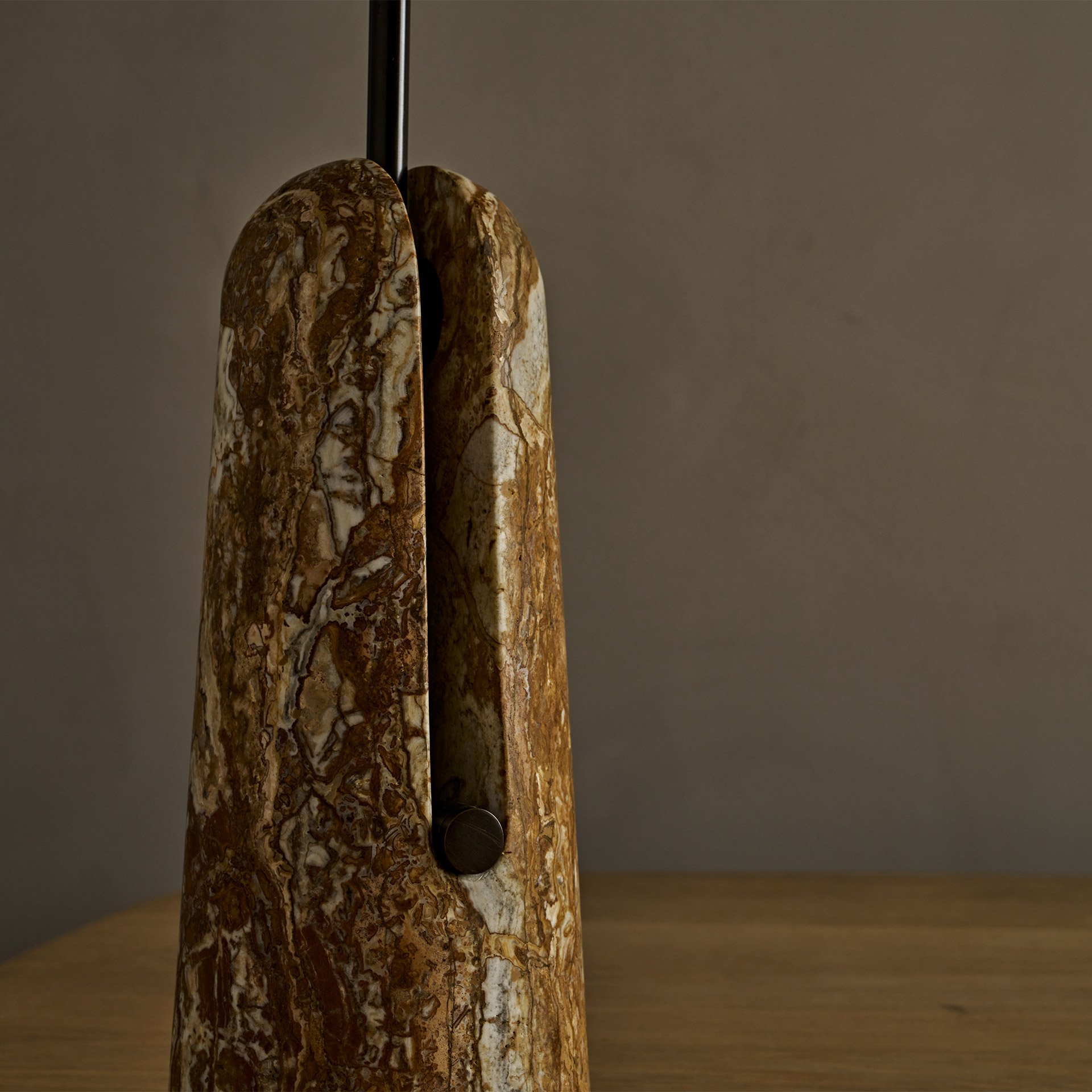 The Malt table lamp embodies unique design with its solid brass support and shade resting within a stone base, creating an intriguing blend of negative space and structural elegance.