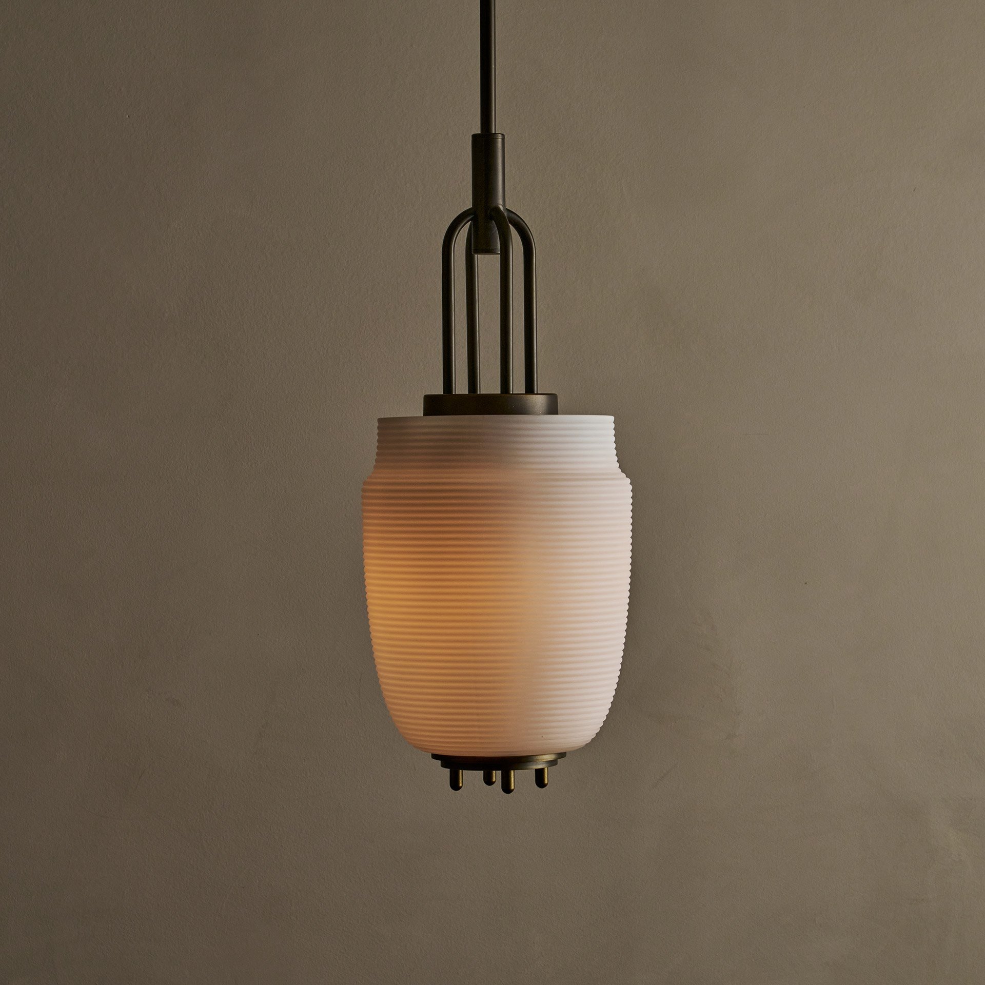 The Milton ceiling pendant embodies fluid design with solid brass and reeded glass elements. Supporting bars extend through, converging at a perforated brass plate for a seamless aesthetic