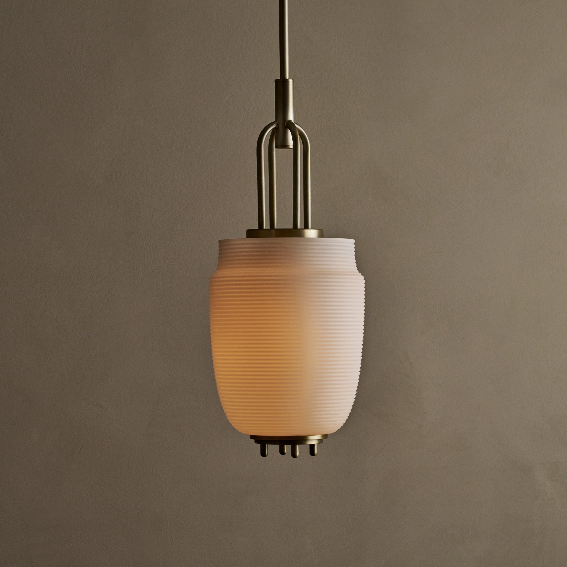 The Milton ceiling pendant embodies fluid design with solid brass and reeded glass elements. Supporting bars extend through, converging at a perforated brass plate for a seamless aesthetic