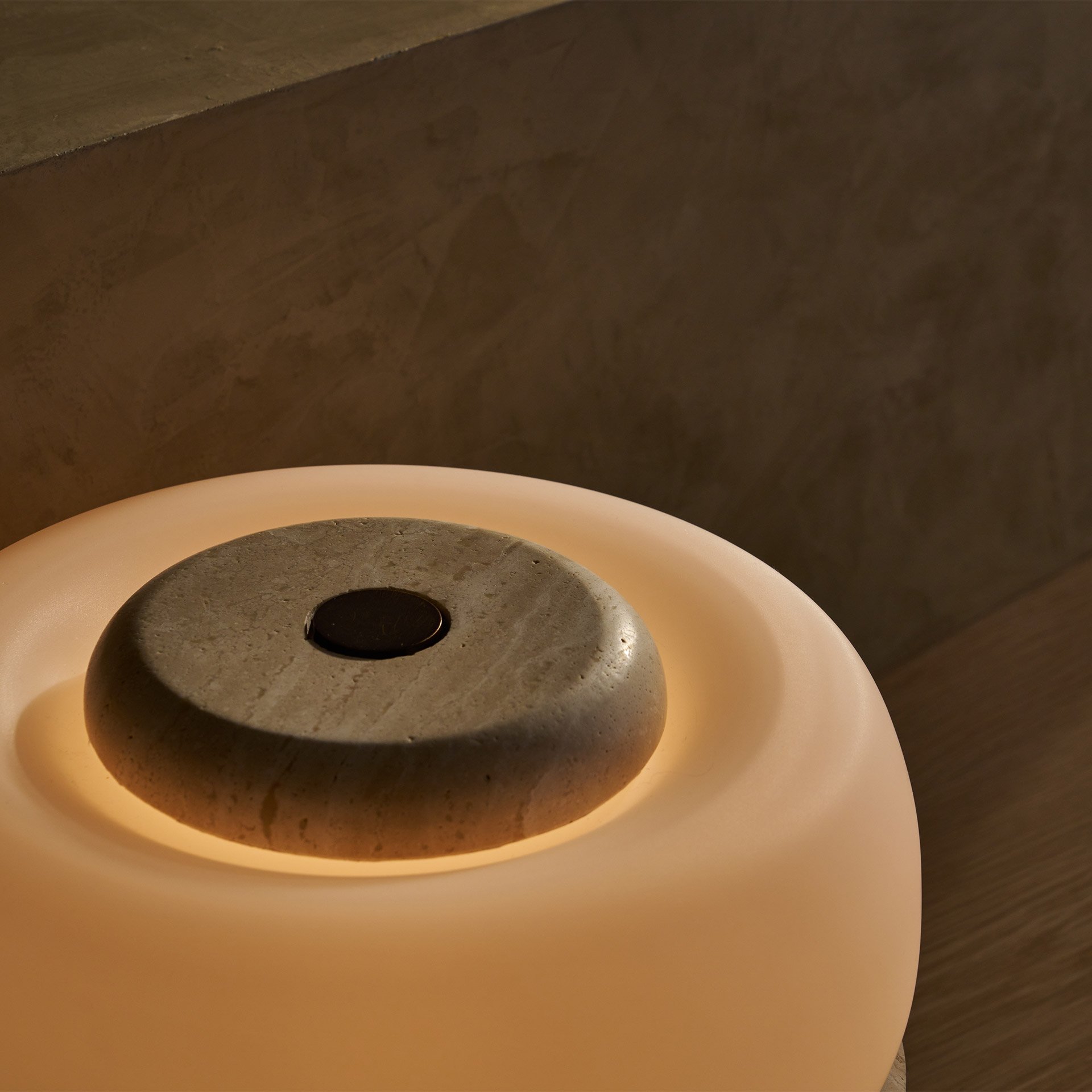 The Ramson table lamp boasts a bulbous stone base with intricate geometric details, complemented by a seamless glass shade. Supported by three tapered solid brass feet.