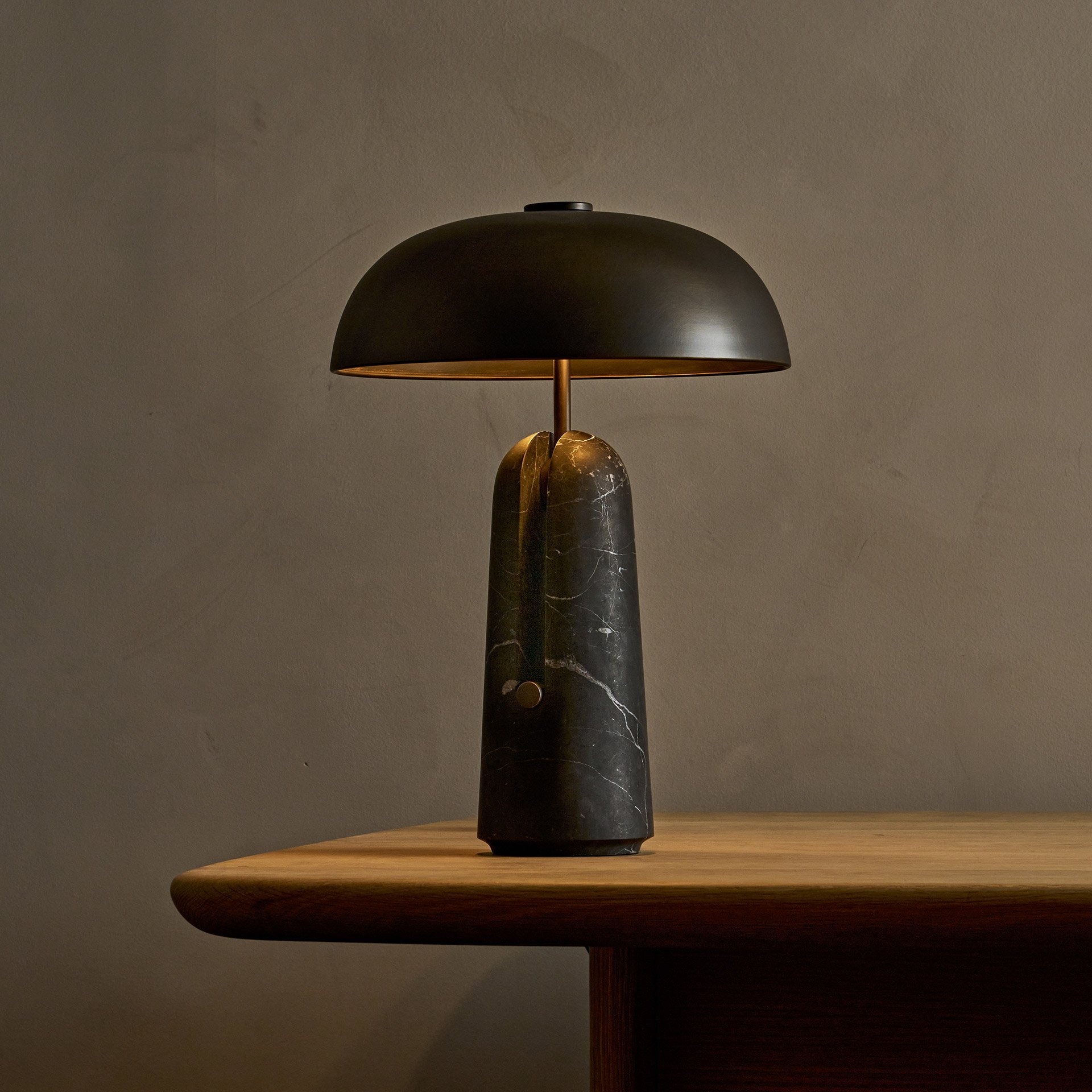The Malt table lamp embodies unique design with its solid brass support and shade resting within a stone base, creating an intriguing blend of negative space and structural elegance.