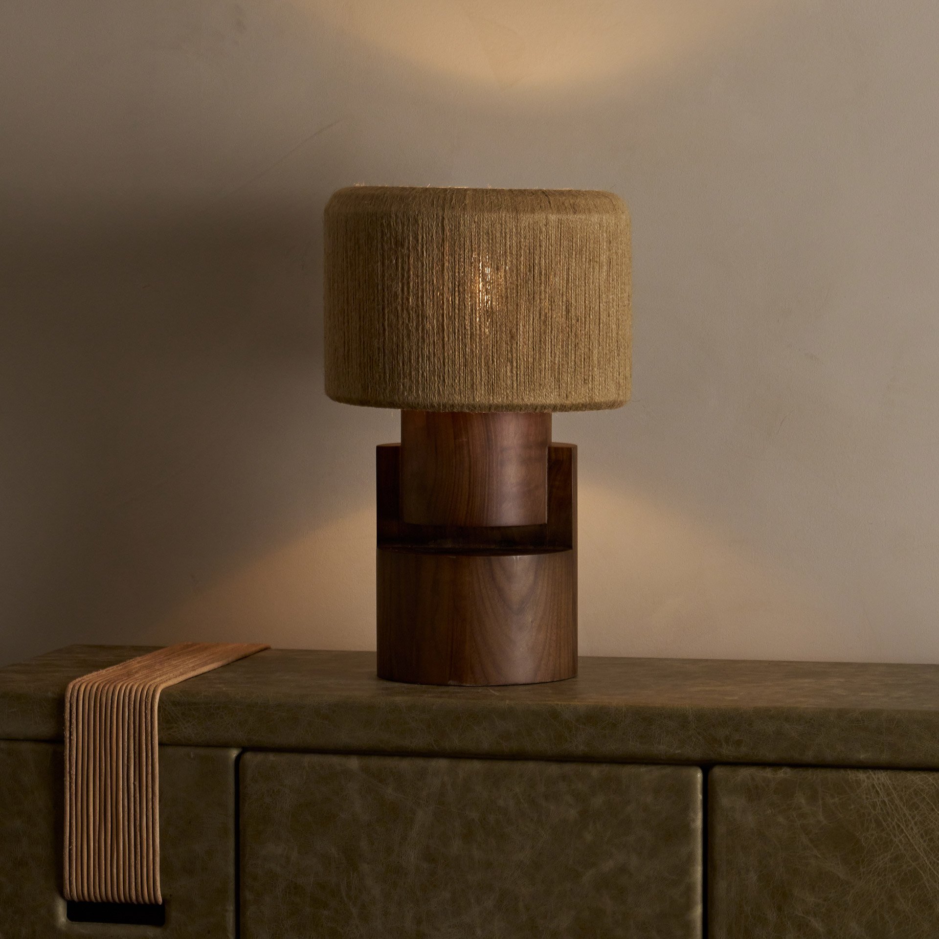 The Stagg table lamp showcases stacked wood cylinders supporting a brass frame with a handwoven string shade, revealing both symmetric and asymmetric forms from different angles