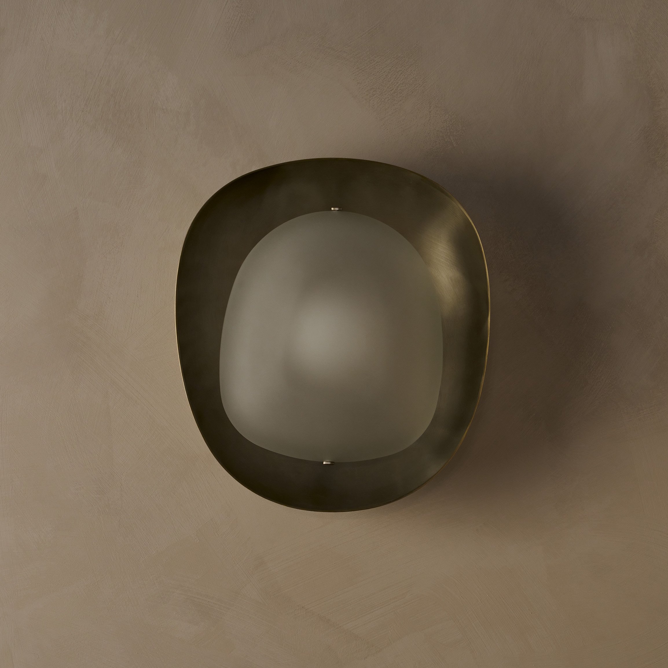 The Dormus Sconce, featuring a brass exterior enclosing an inverted glass shade of matching shape, showcasing a striking interplay of negative space within the elegant design.