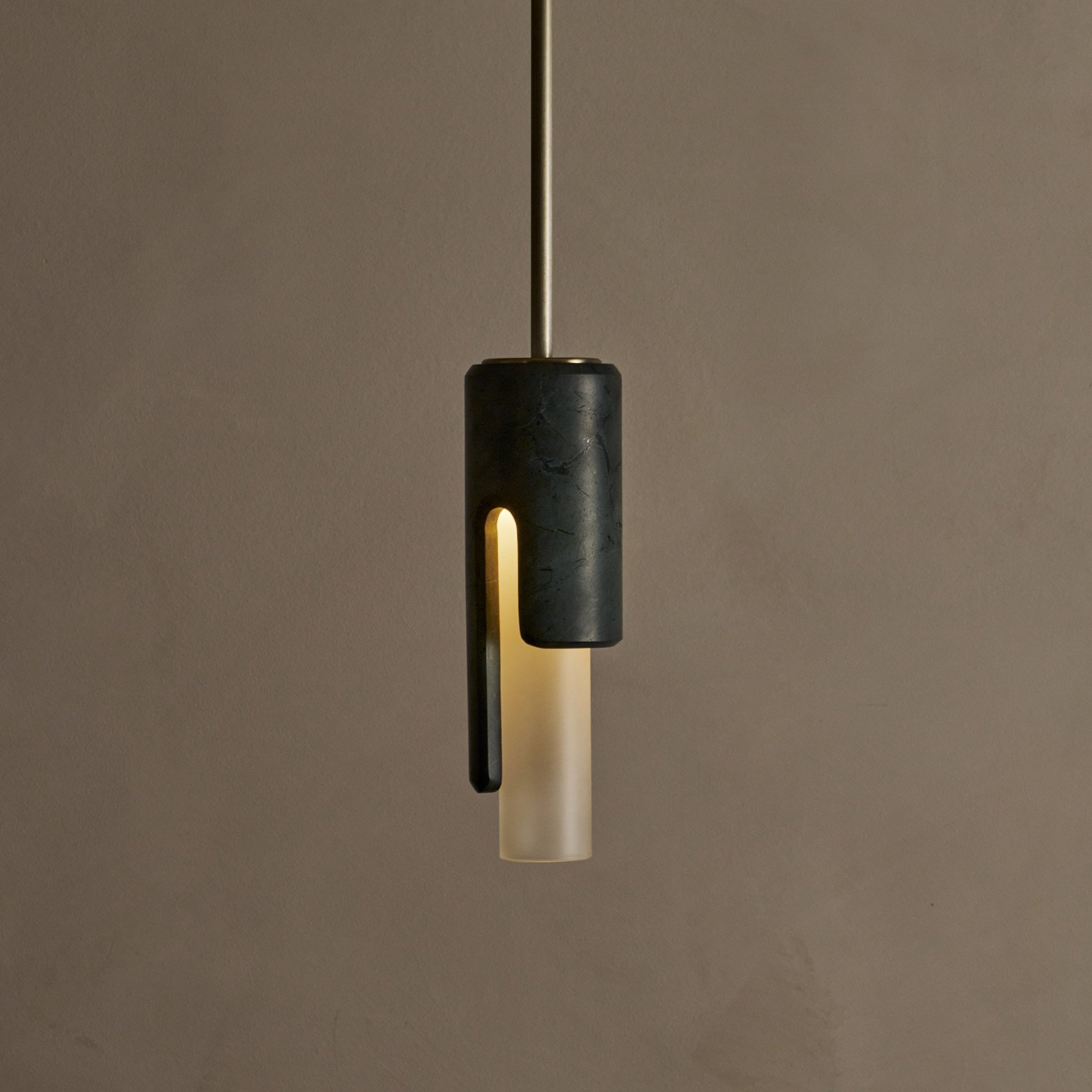 The Dover ceiling pendant features hidden fastening, seamlessly blending stone and glass components. Its cylindrical shade reveals an asymmetric profile from the side.