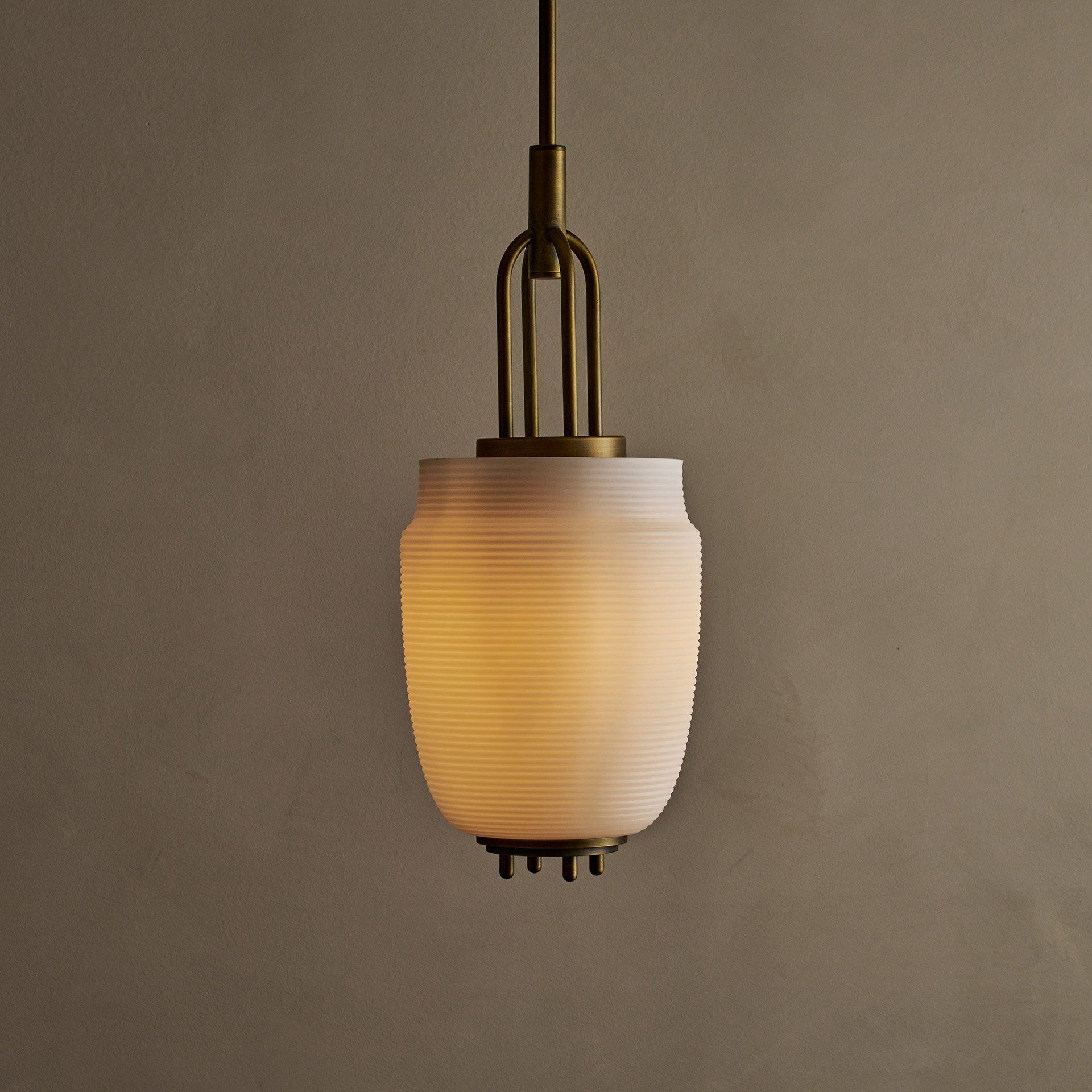The Milton ceiling pendant embodies fluid design with solid brass and reeded glass elements. Supporting bars extend through, converging at a perforated brass plate for a seamless aesthetic