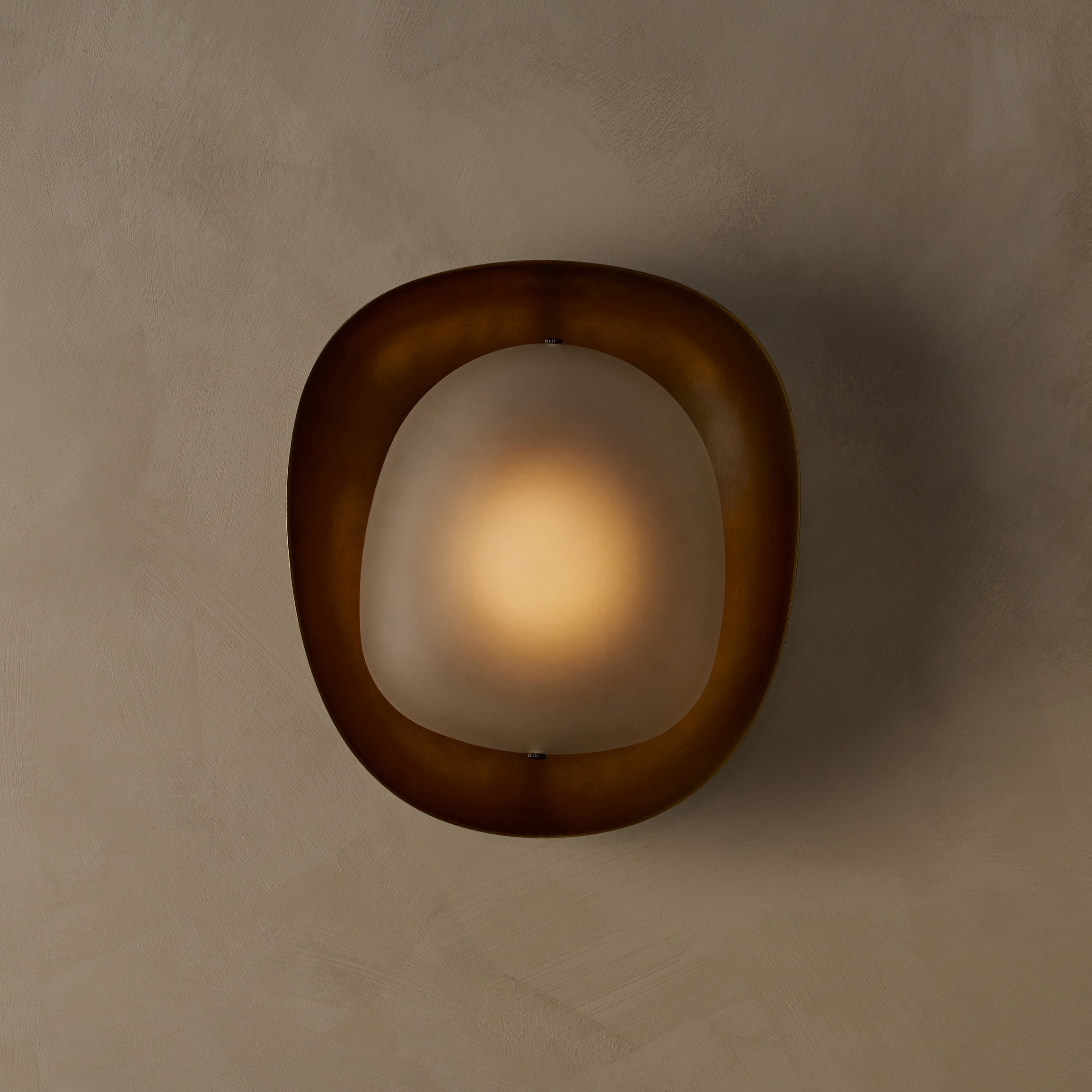 The Dormus Sconce, featuring a brass exterior enclosing an inverted glass shade of matching shape, showcasing a striking interplay of negative space within the elegant design.