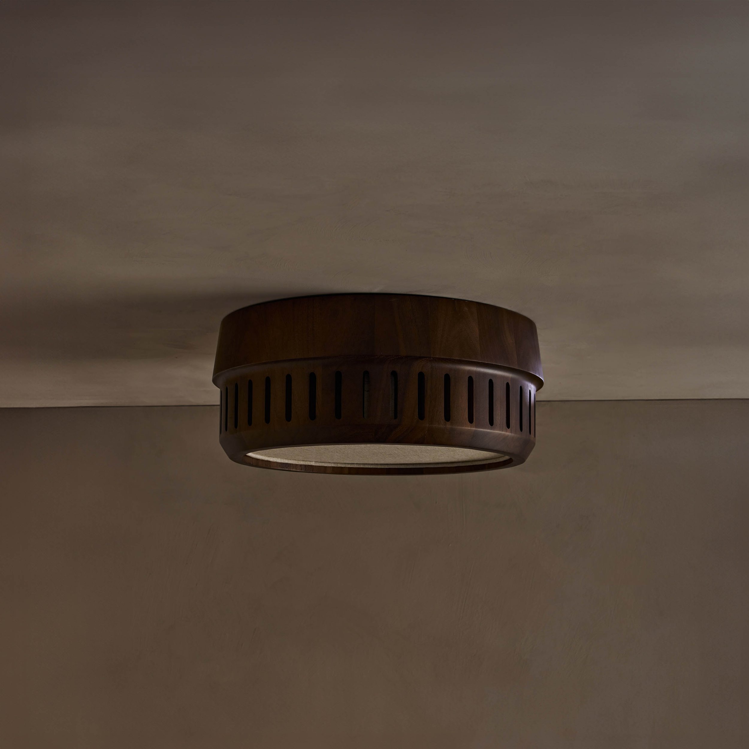 The Adler ceiling mount nests a linen drum shade within a solid wood exterior, offering functional downward illumination. Notches in the wood allow glimpses of the fabric shade within.