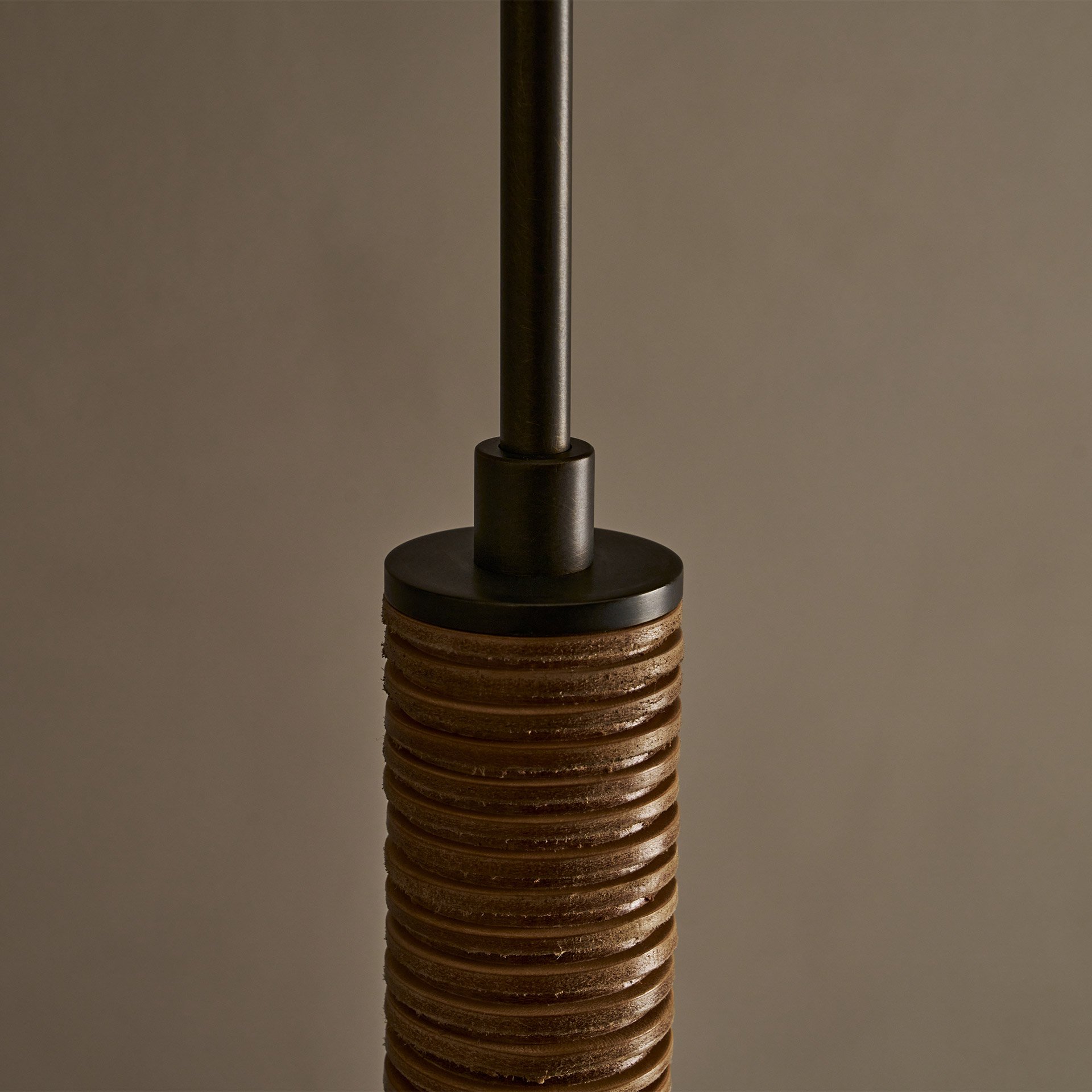 The Pell pendant lamp features a solid body crafted from stacked leather hide disks, showcasing the natural imperfections of the material's edge. A frosted glass sphere hangs at the bottom